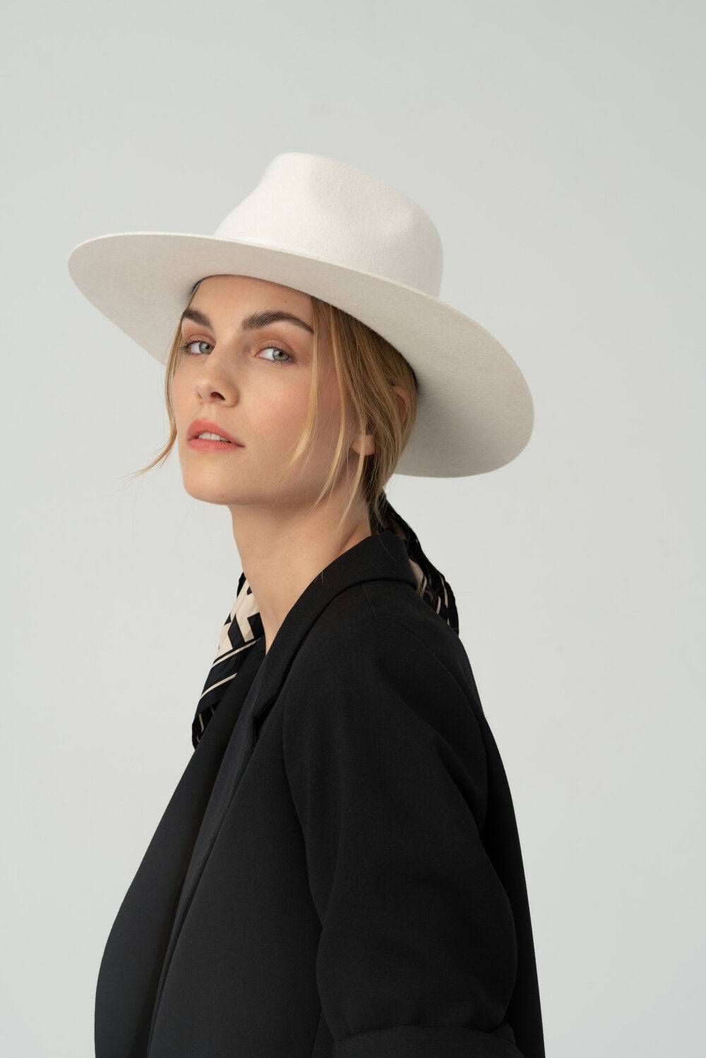 Classic ivory fedora hat with monogram embellishment, styled with a black blazer and silk scarf for a refined, high-fashion look.