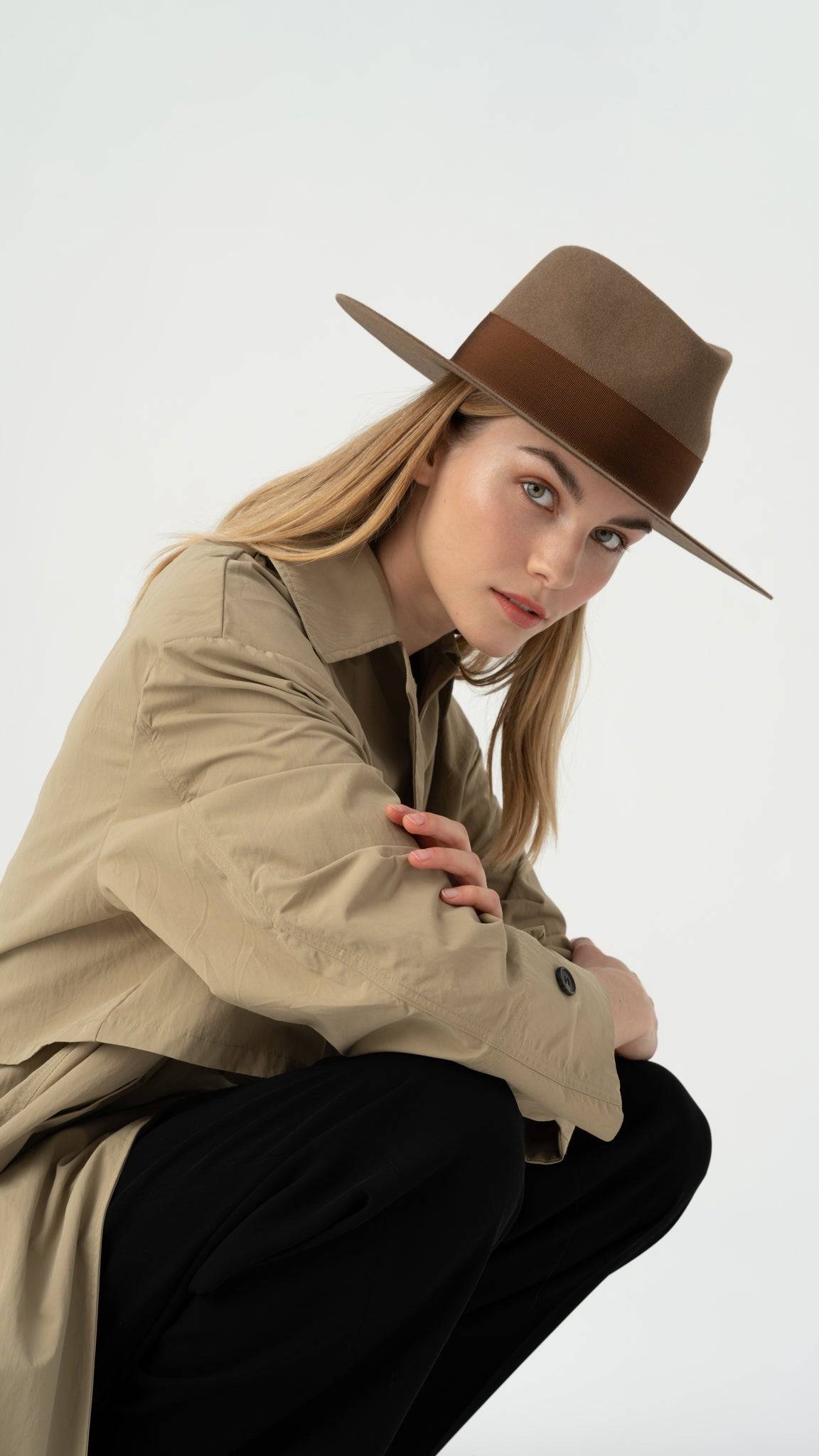 Stylish walnut fedora hat with an 8.5 cm brim and brown band, worn by a model in a beige trench coat. Handcrafted from 100% rabbit fur felt.