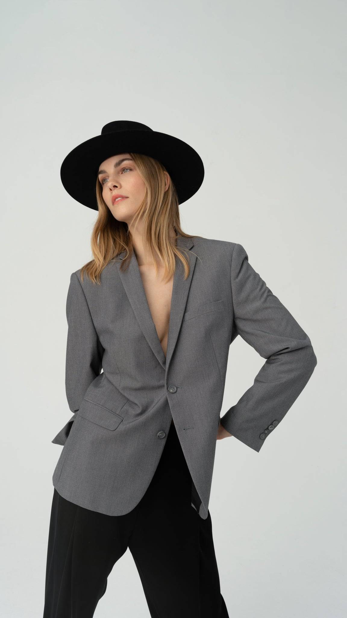Elegant black fedora hat with a leather band and monogram accent, paired with a gray blazer. A high-fashion statement piece. Order now with a discount.