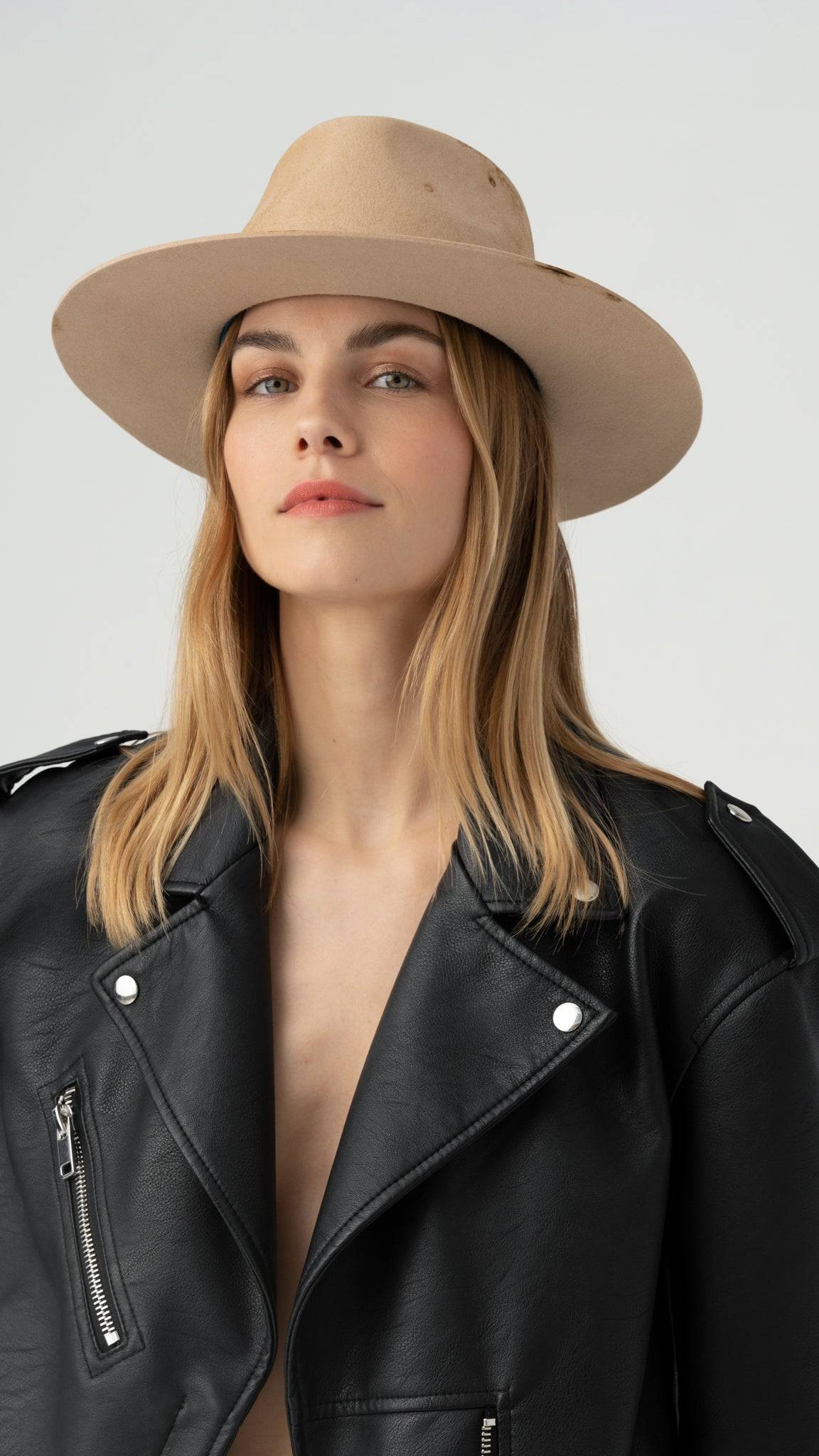 Close-up of a distressed nude fedora hat worn with a black leather jacket. Luxury designer fedora made from rabbit fur felt with unique detailing.