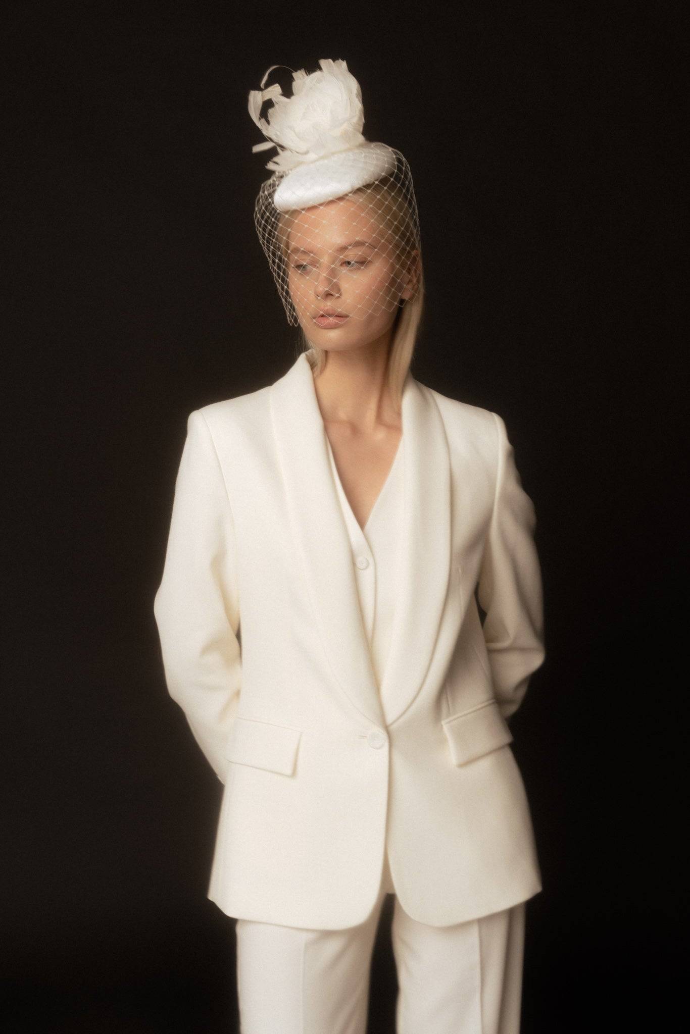 Bridal cocktail hat with feather flower, featuring a vintage-inspired birdcage veil. Elegant white silk headpiece, perfect for weddings and couture styling.