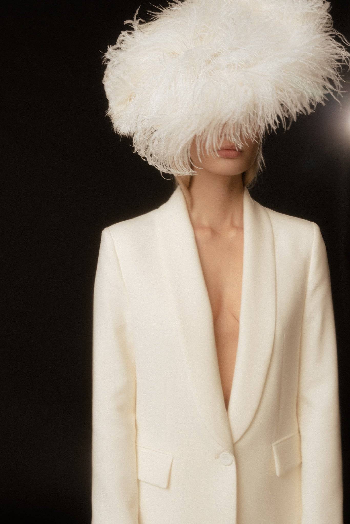Luxurious ostrich feathered headpiece in white, styled with an elegant cream blazer. A statement bridal accessory for a couture wedding look.