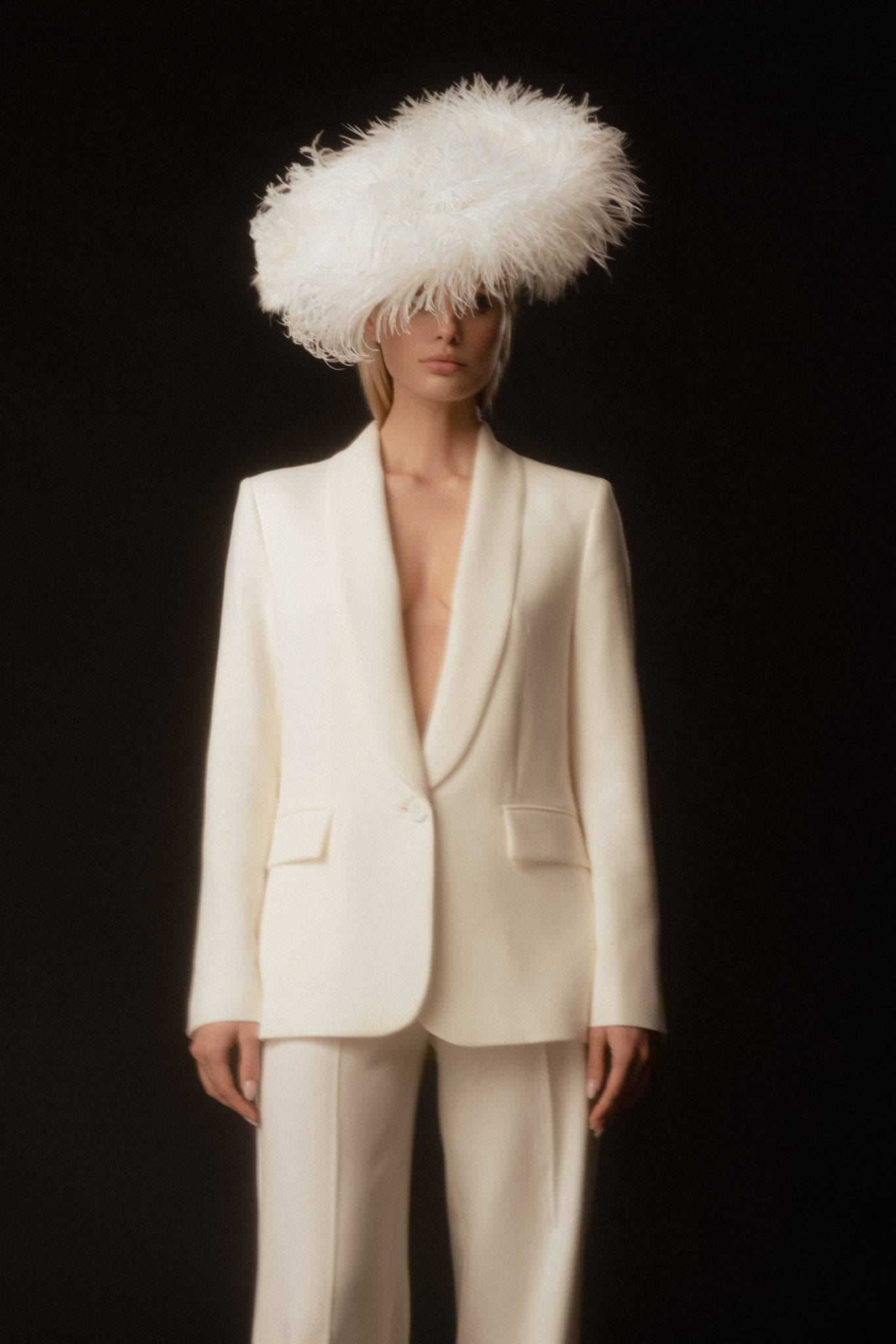 Chic bridal ensemble featuring a white ostrich feathered headpiece and tailored cream suit. A modern take on wedding fashion with vintage charm.