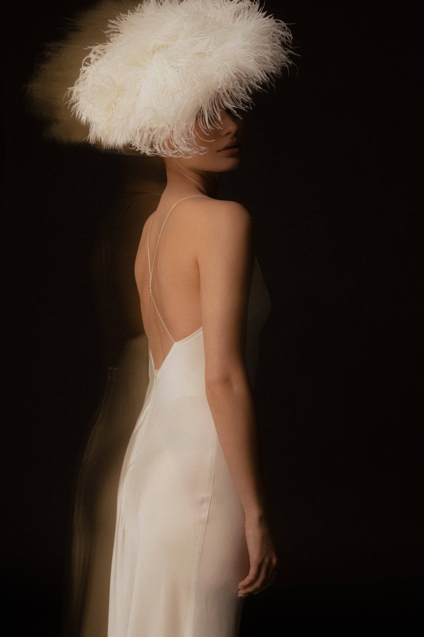 Elegant bride wearing a white silk gown and ostrich feathered headpiece. A luxury bridal hair accessory for a sophisticated wedding style.