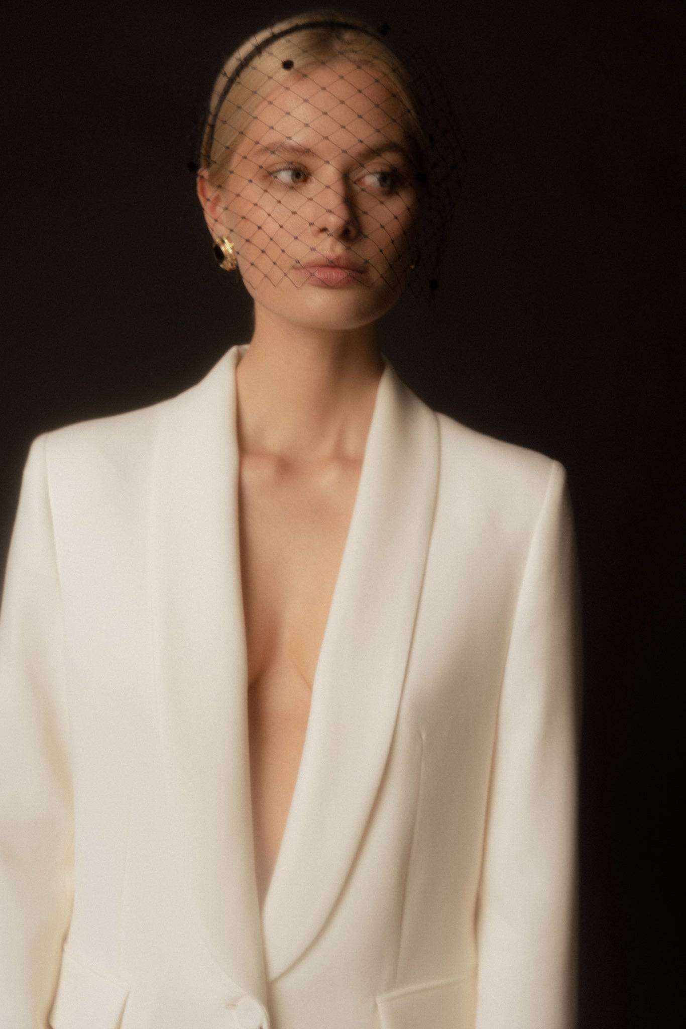 Close-up of black veil-detail satin silk headband styled with a white blazer. A chic and timeless event accessory.