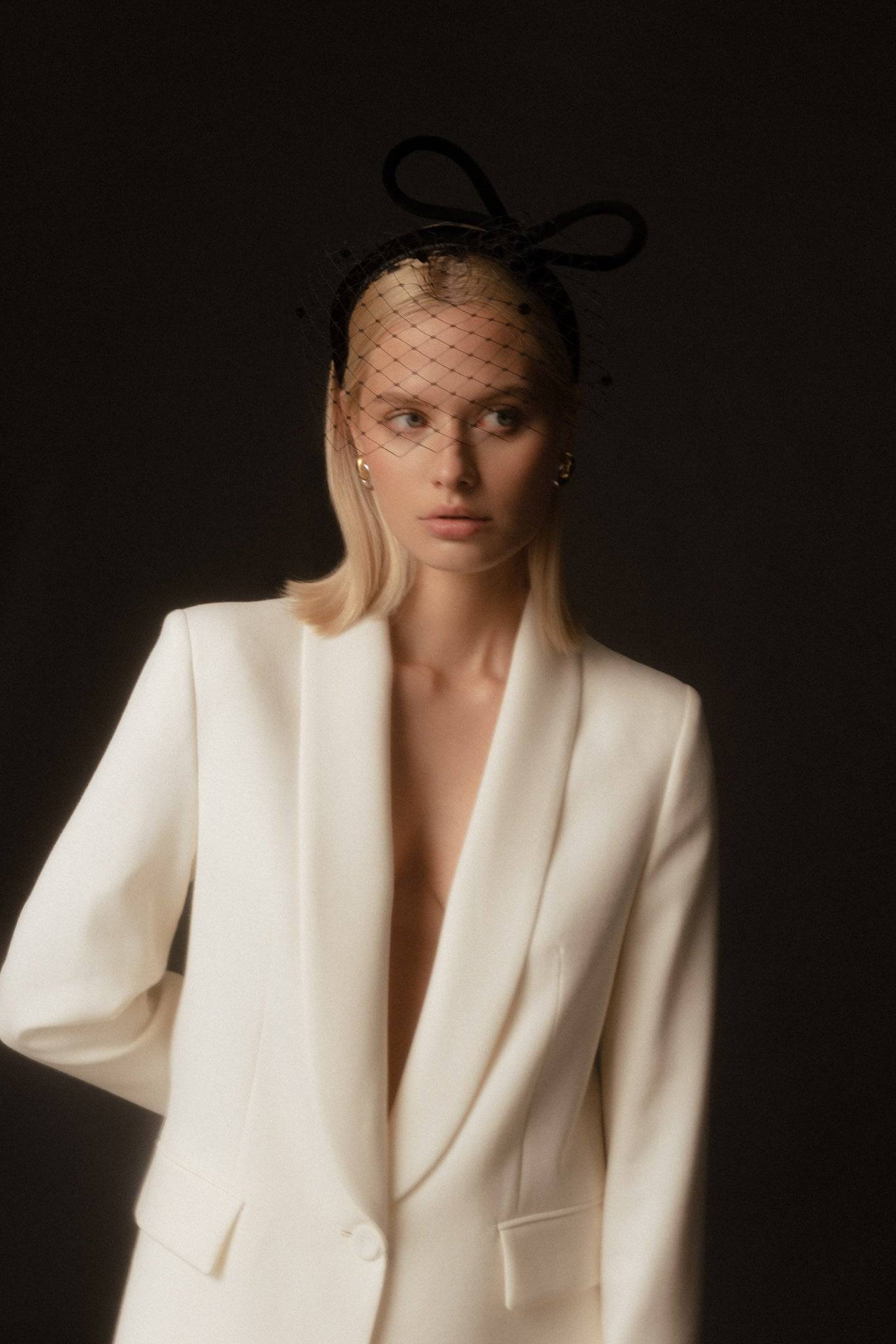 Close-up of a black bow embellished headband with veil, adding a touch of retro glamour to a sleek white suit ensemble.