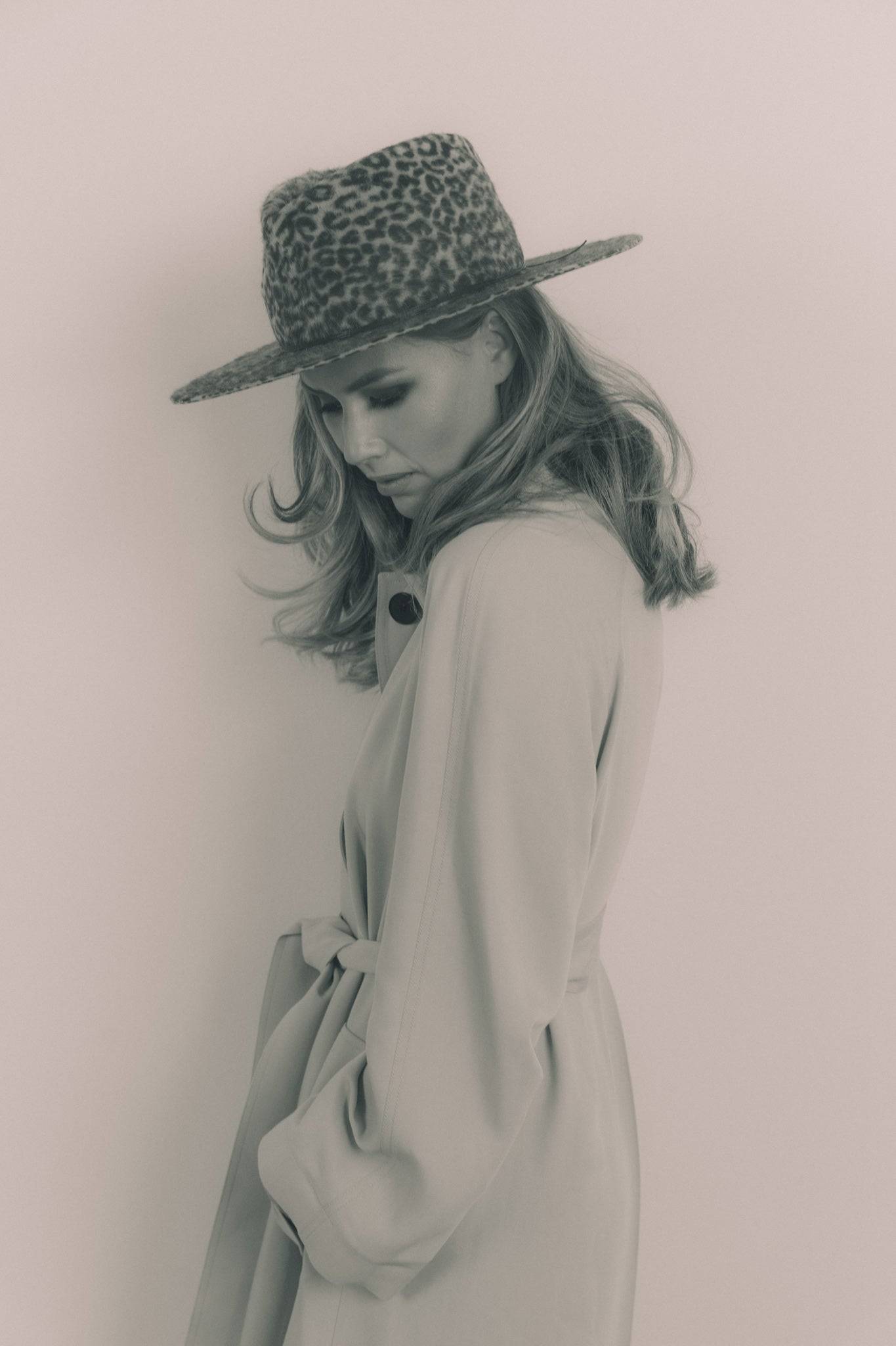 Side profile of a woman wearing a grey leopard print fedora hat with a beige coat. A timeless and stylish fashion statement. Order yours today.