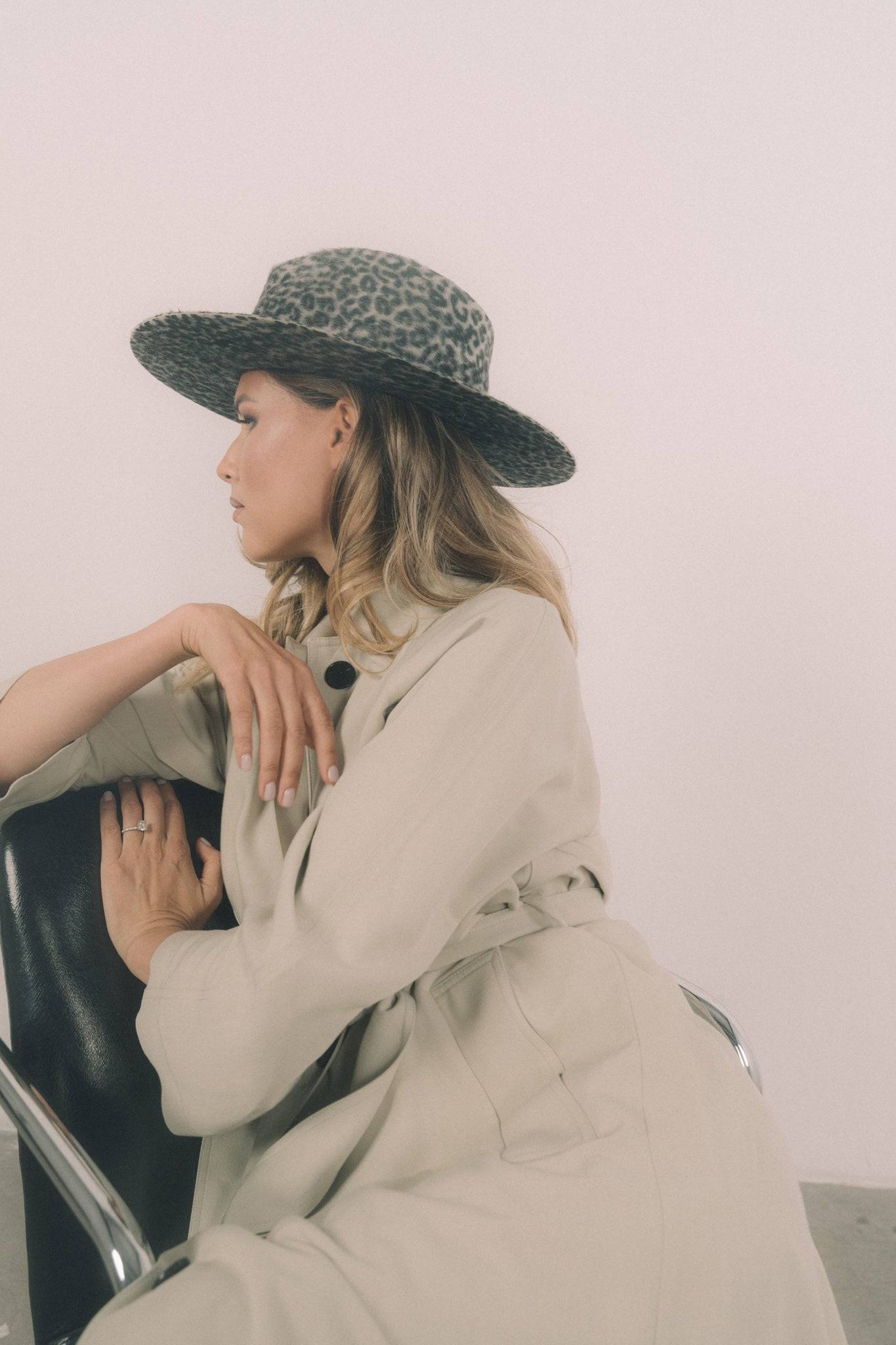 Stylish grey leopard print fedora hat paired with a beige coat, captured in a relaxed pose. A unique fashion accessory for any wardrobe. Shop today.