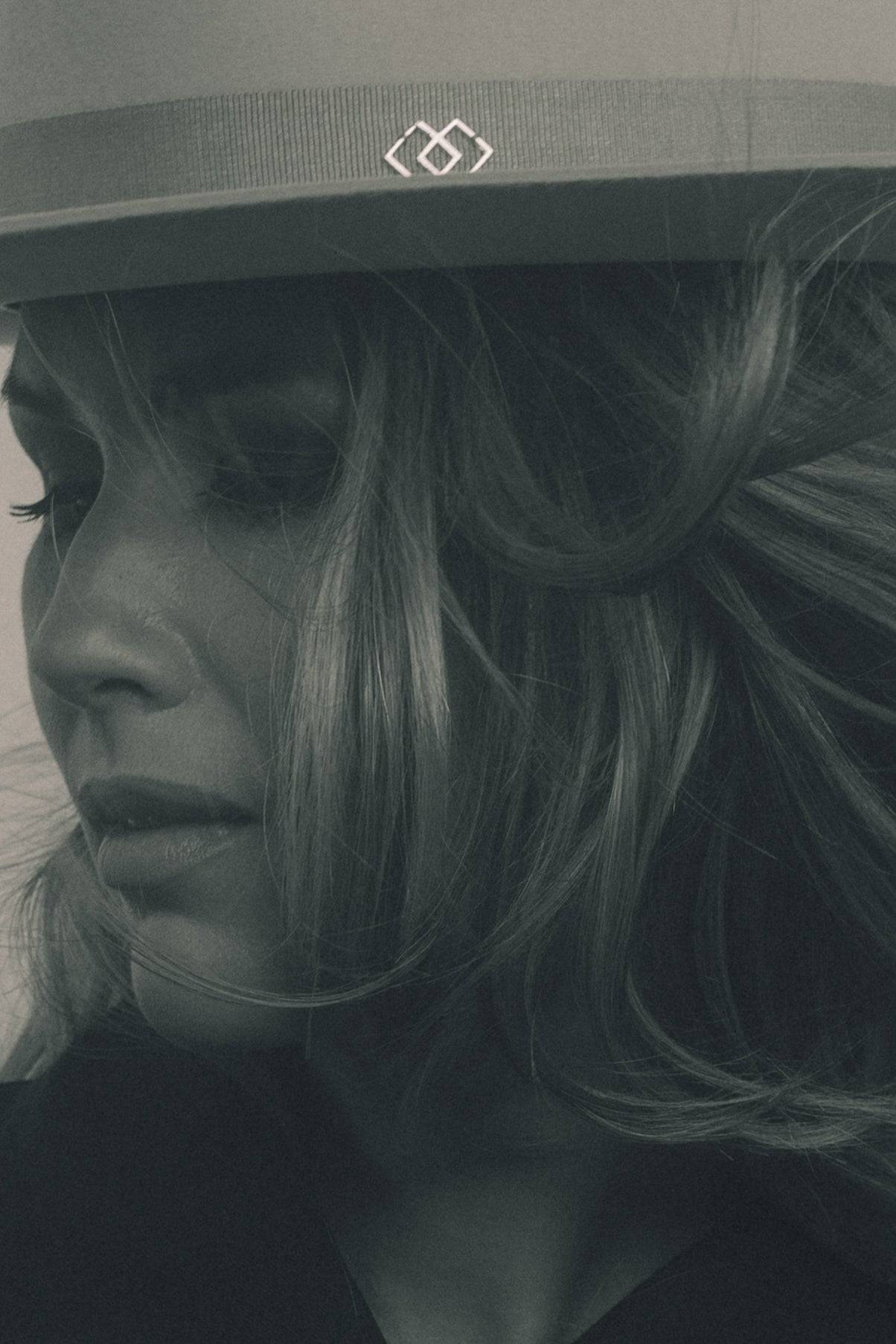 Close-up of a light grey fedora hat featuring a monogram embellishment on the ribbon. A luxury handcrafted rabbit fur felt hat.