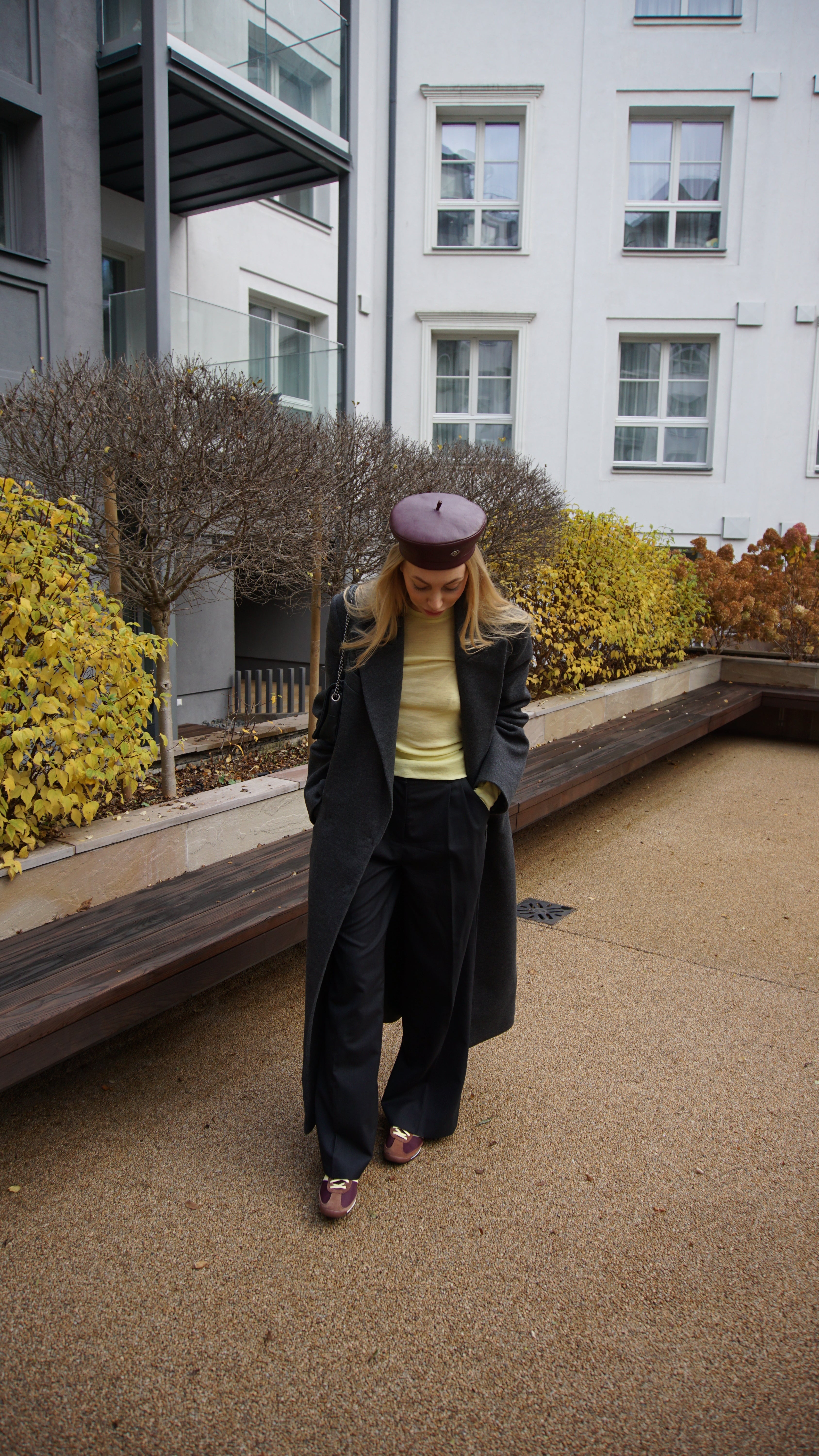 Woman wearing a burgundy leather beret with a long gray coat and wide-leg trousers. A stylish statement piece for sophisticated street style.