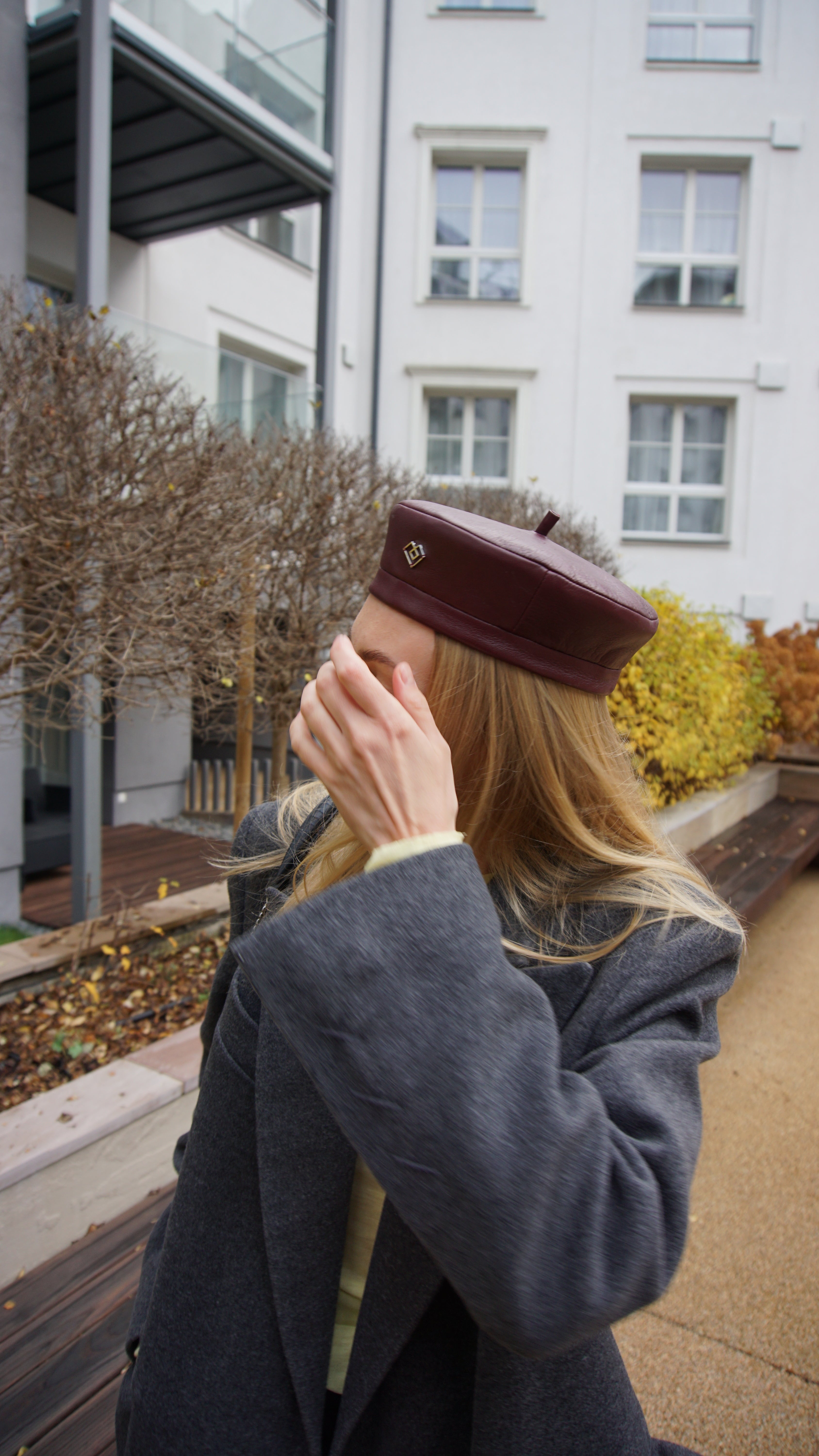 Burgundy leather beret styled with a dark gray coat and yellow sweater. Chic Parisian-inspired fashion accessory for a modern, elegant look.