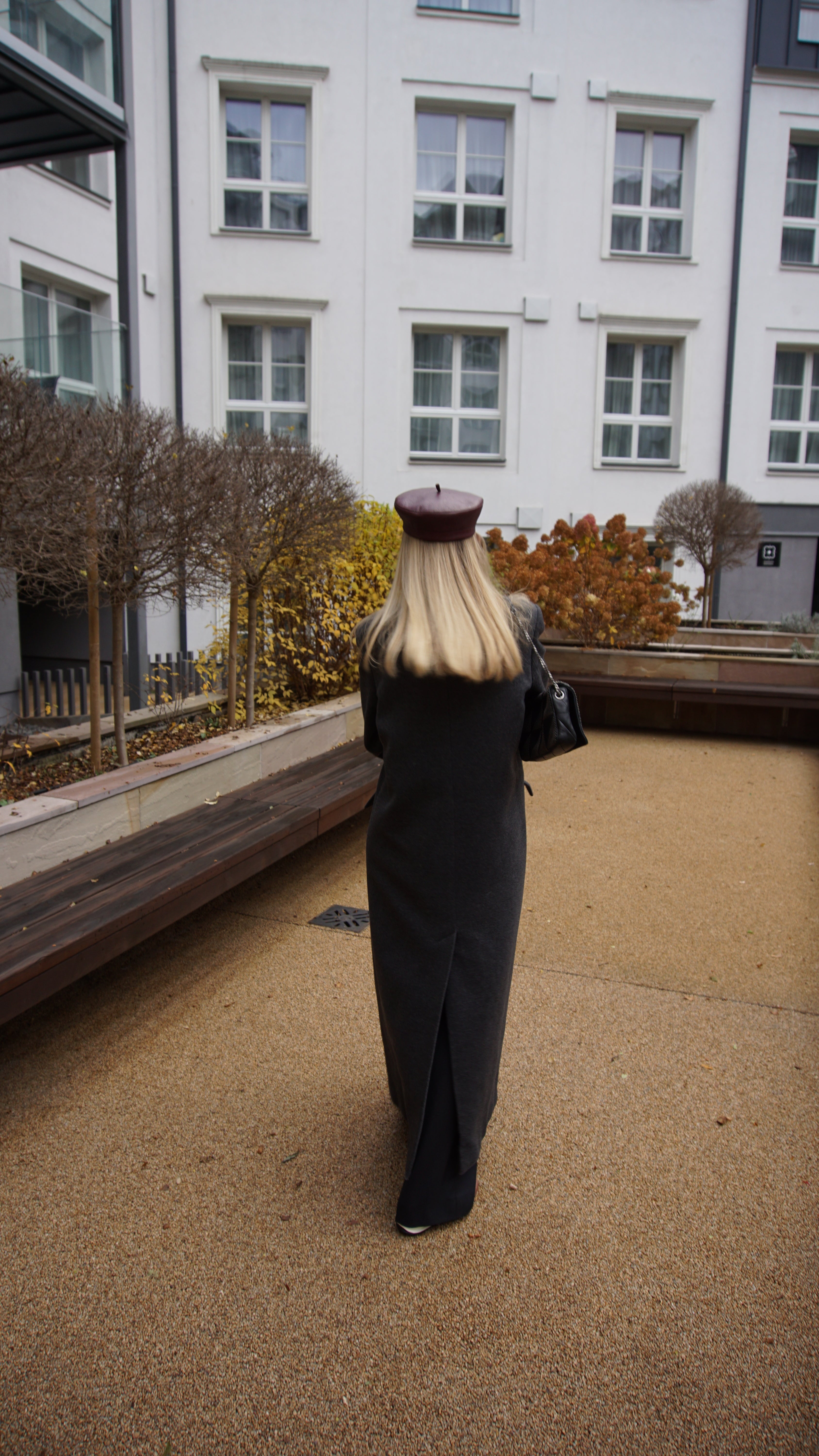 Back view of a woman in a burgundy leather beret and long gray coat. A timeless and trendy leather accessory for a refined fashion statement.
