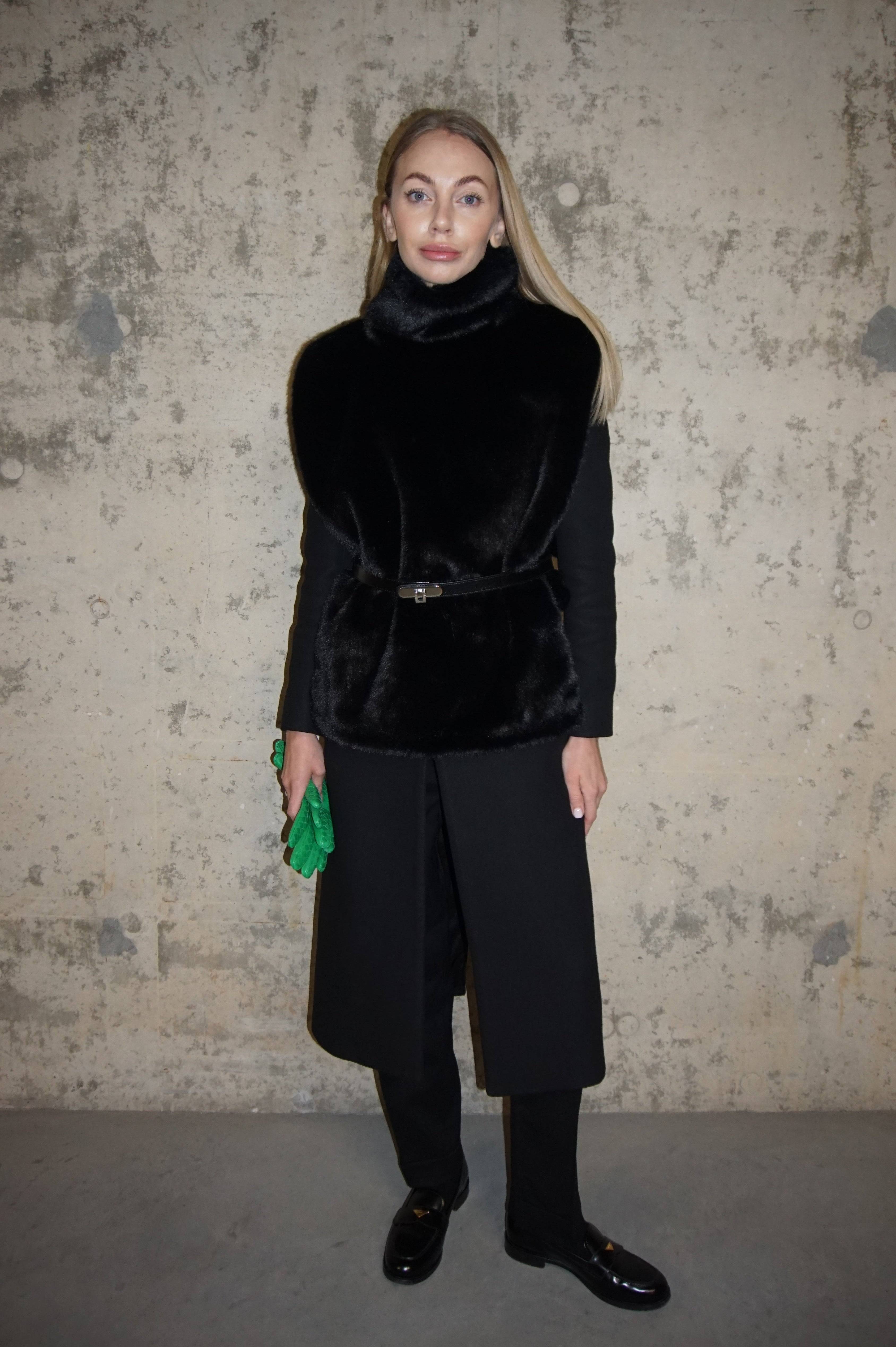Black faux fur turtleneck styled with a sleek black coat and trousers, accessorized with a green clutch. A chic winter layering piece for elegance and warmth.