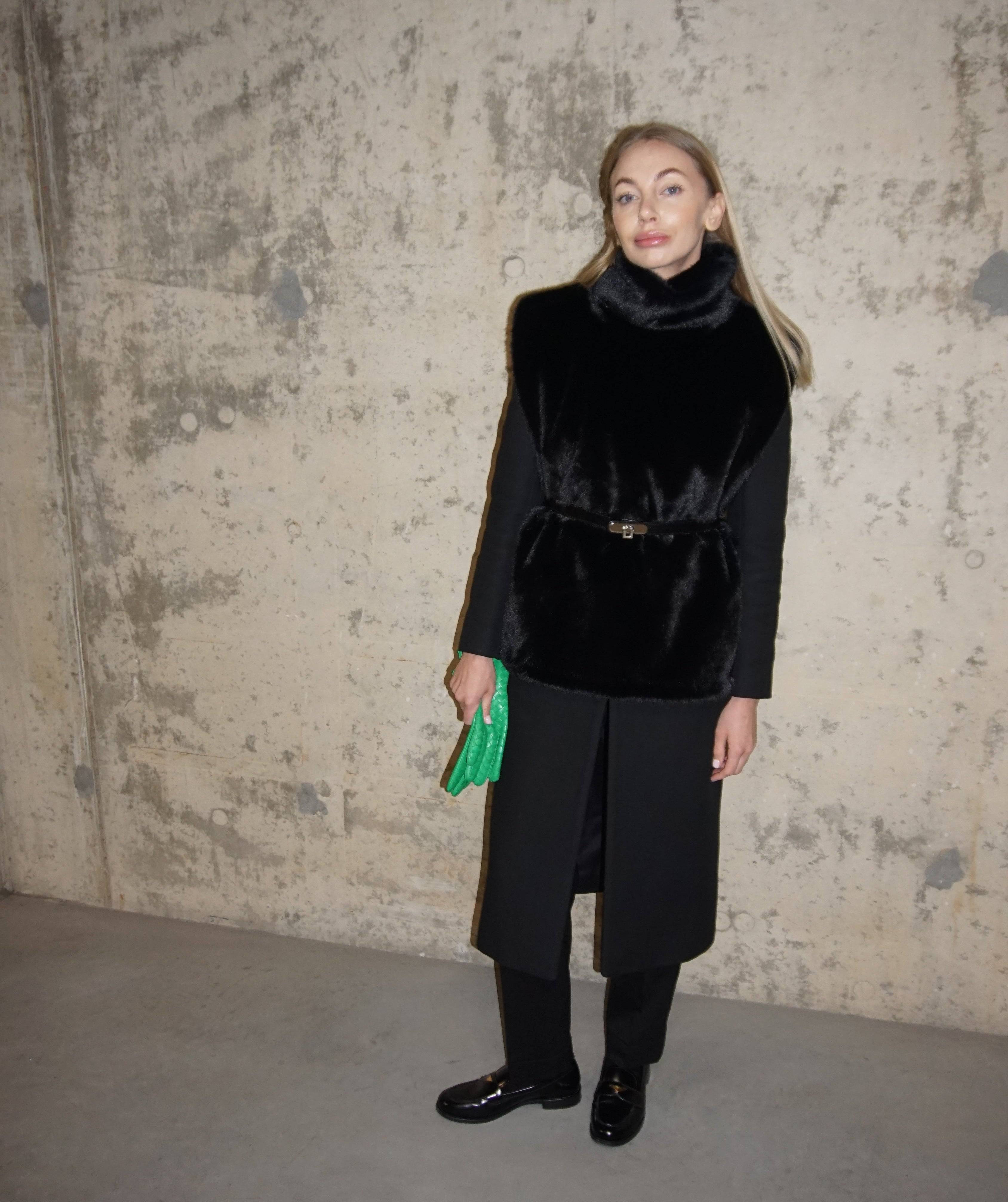 Elegant black faux fur turtleneck layered over a black coat, complemented by a green clutch. A fashionable winter accessory for warmth and style.