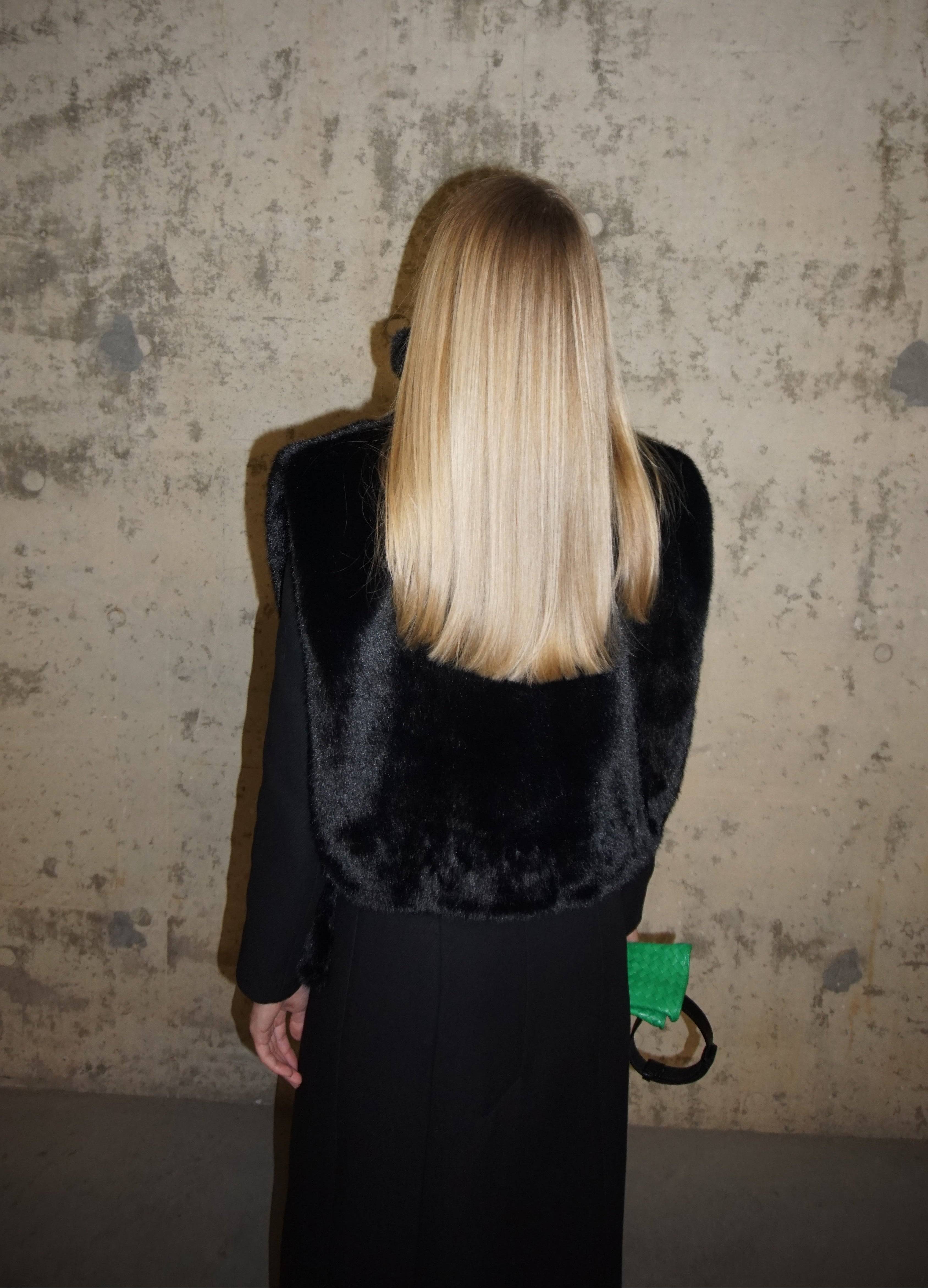 Back view of a black faux fur turtleneck draped over a black coat. A plush and stylish winter layering piece for a refined cold-weather look.