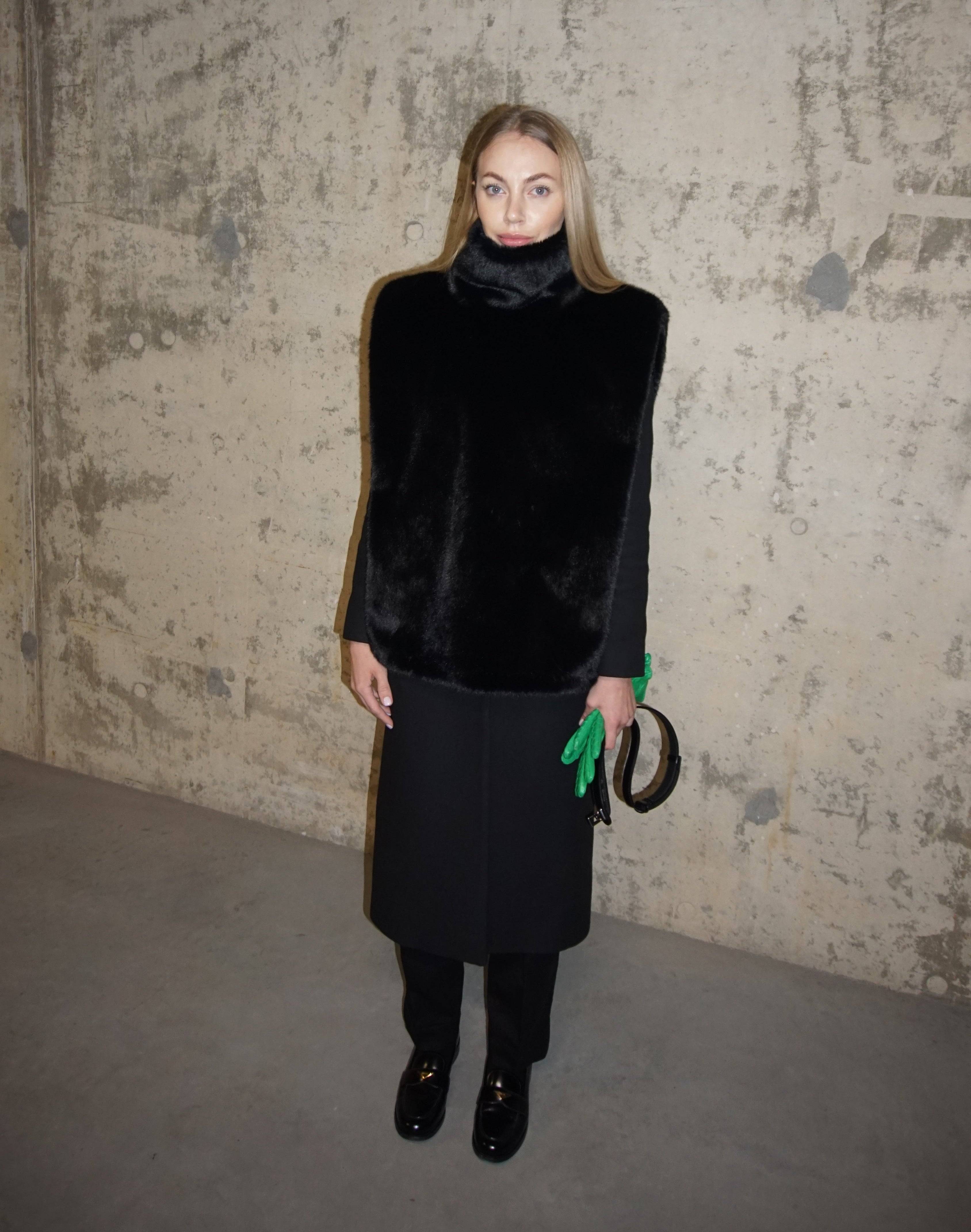 Plush black faux fur turtleneck styled with a black coat and trousers, accessorized with a green clutch. A luxurious winter staple for warmth and elegance.