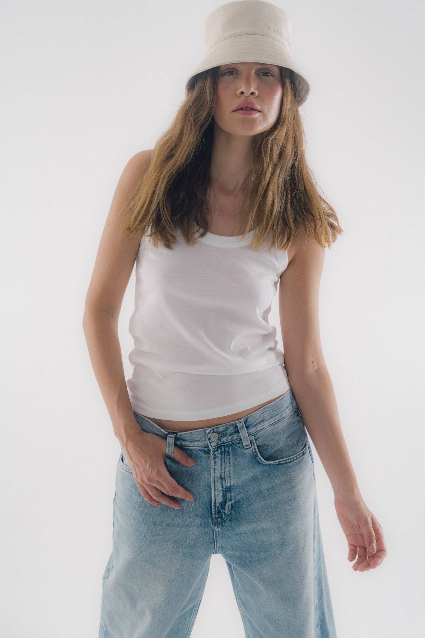 Light beige denim bucket hat paired with a white tank top and jeans. A versatile, travel-ready fashion piece for effortless styling.