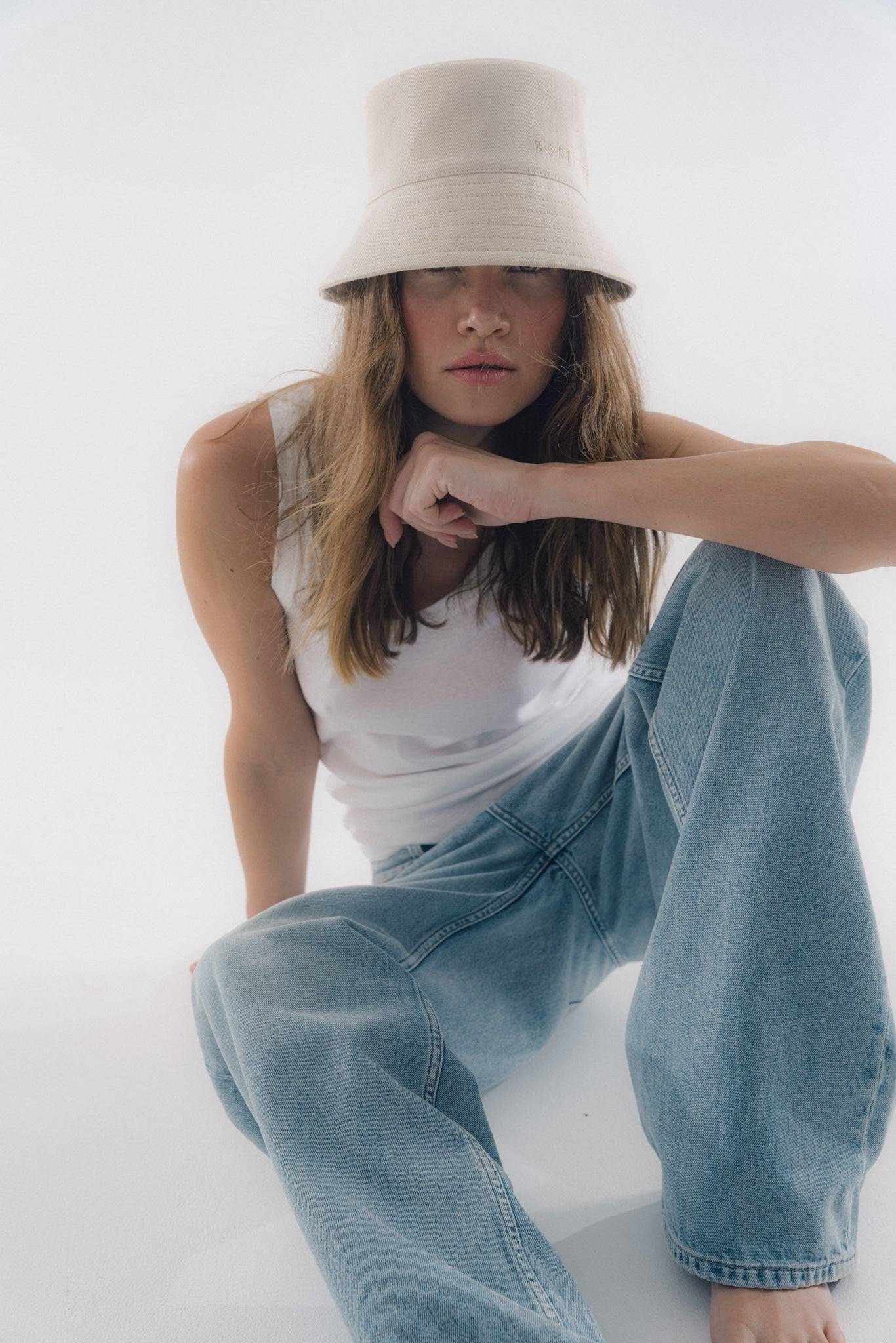 Cotton denim bucket hat in light beige, styled with a white tank top. A high-fashion headwear piece for a chic, effortless look.