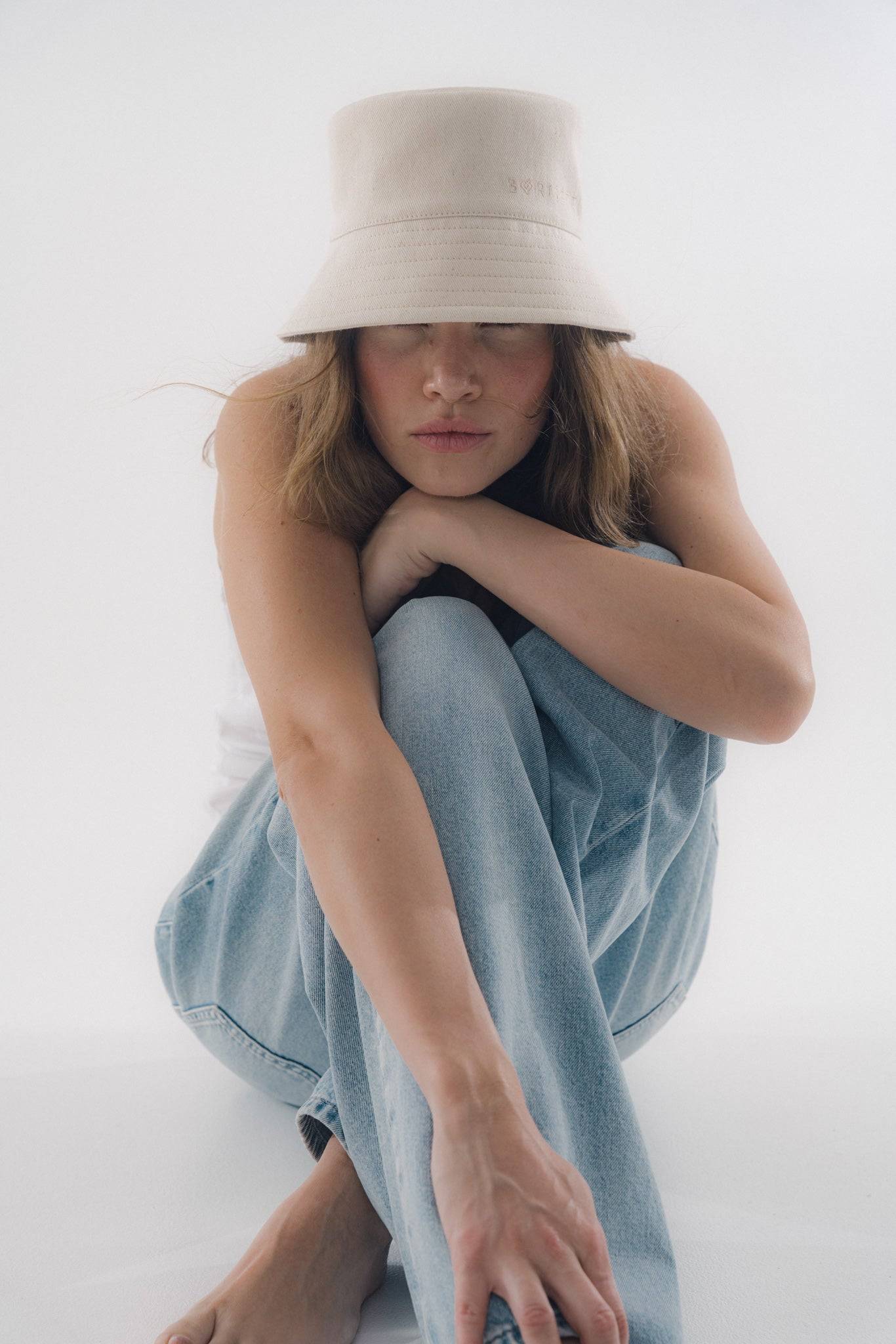 Minimalist beige bucket hat styled with relaxed denim and a white tank top. A perfect blend of comfort and fashion for a laid-back look.