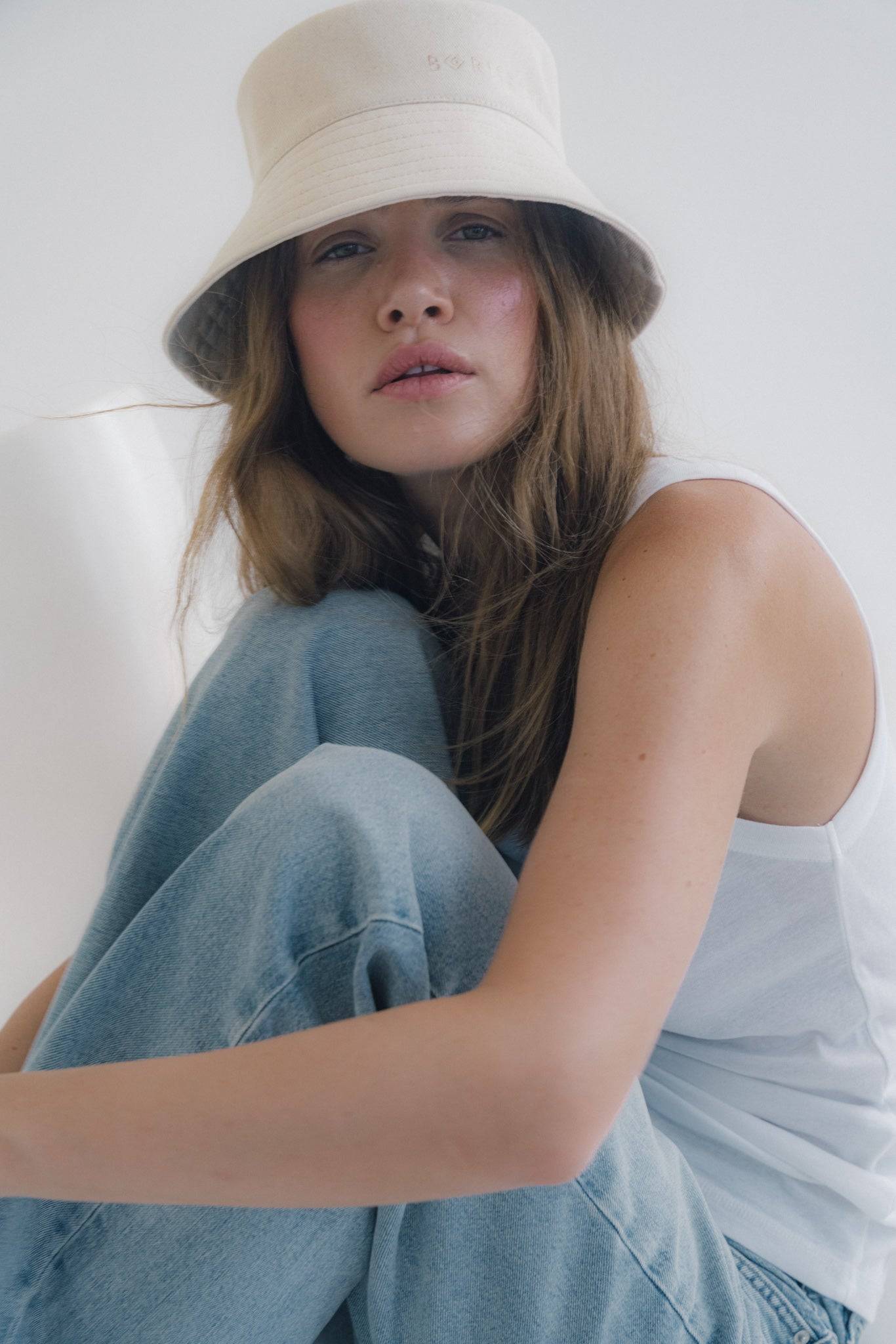 Embroidered beige bucket hat styled with a white tank top. A timeless summer hat for effortless elegance and everyday fashion.