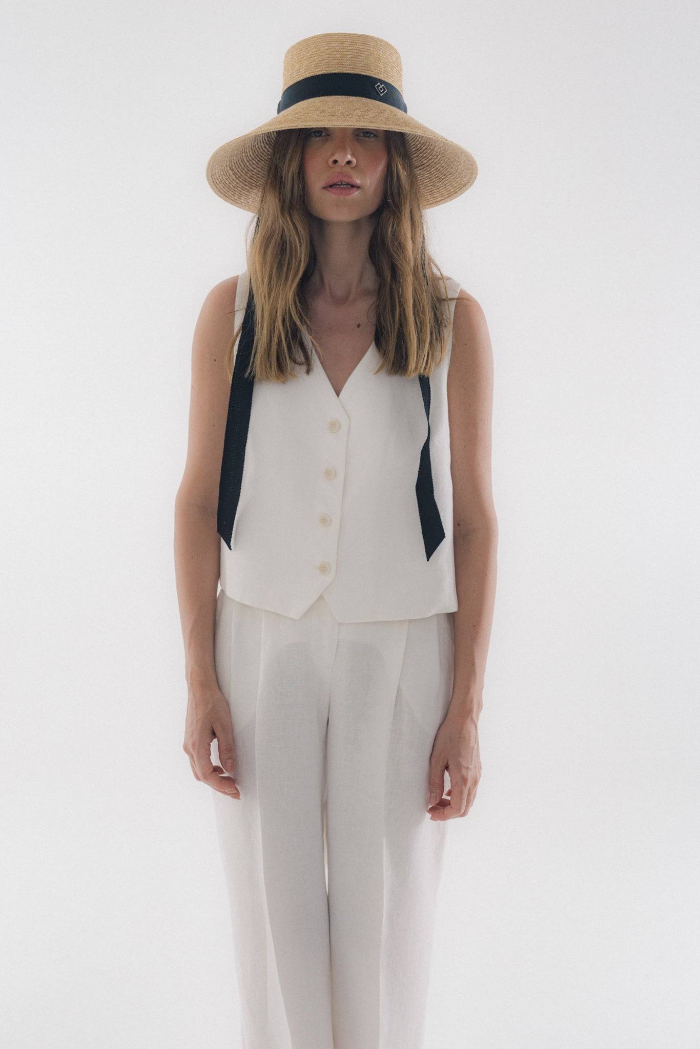Chic neck tie wide brimmed straw hat with black ribbon, elegantly worn by a woman in a white outfit. Perfect for summer fashion and sun protection.