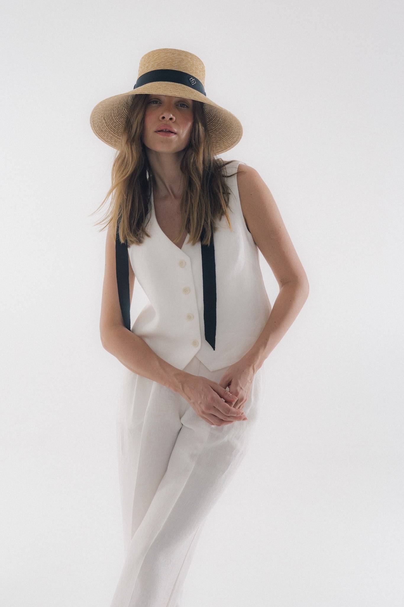 Chic neck tie wide brimmed straw hat with a black ribbon, elegantly worn by a woman in a white outfit. Perfect for summer fashion and sun protection.