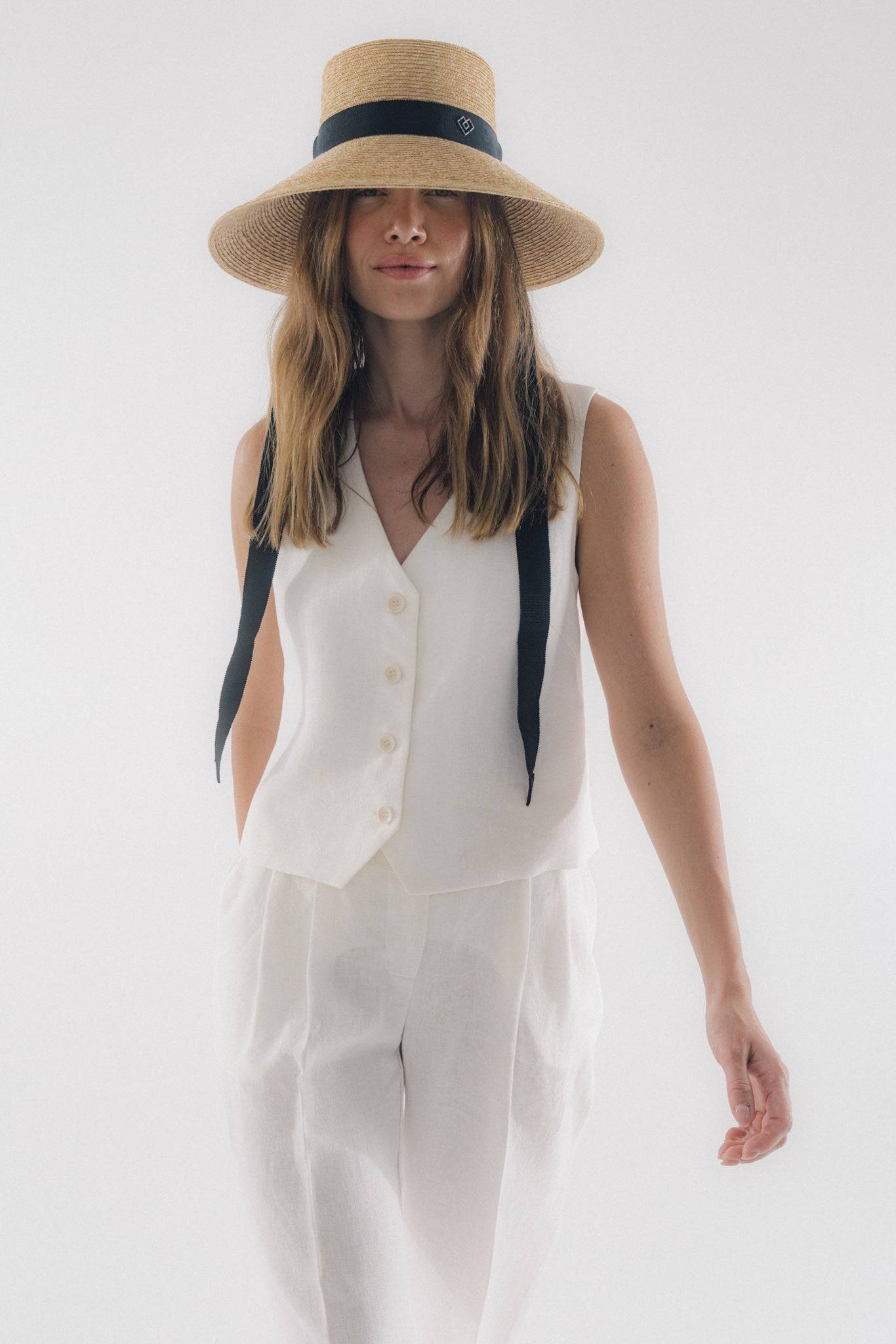 Chic neck tie wide brimmed straw hat with a black ribbon, elegantly worn by a woman in a white linen outfit. Perfect for summer fashion and sun protection.
