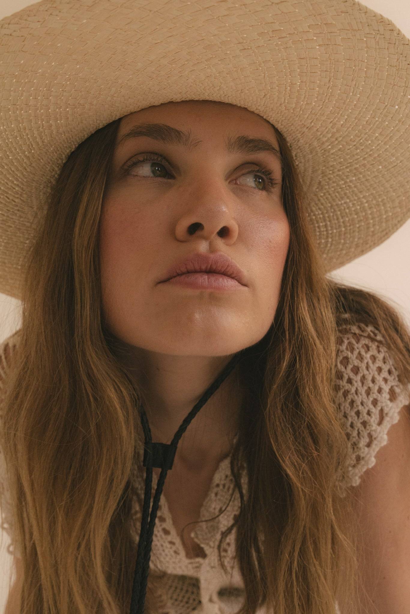Close-up of a woman gazing upwards while wearing a wide-brim straw fedora with a leather strap. A stylish and protective summer hat.