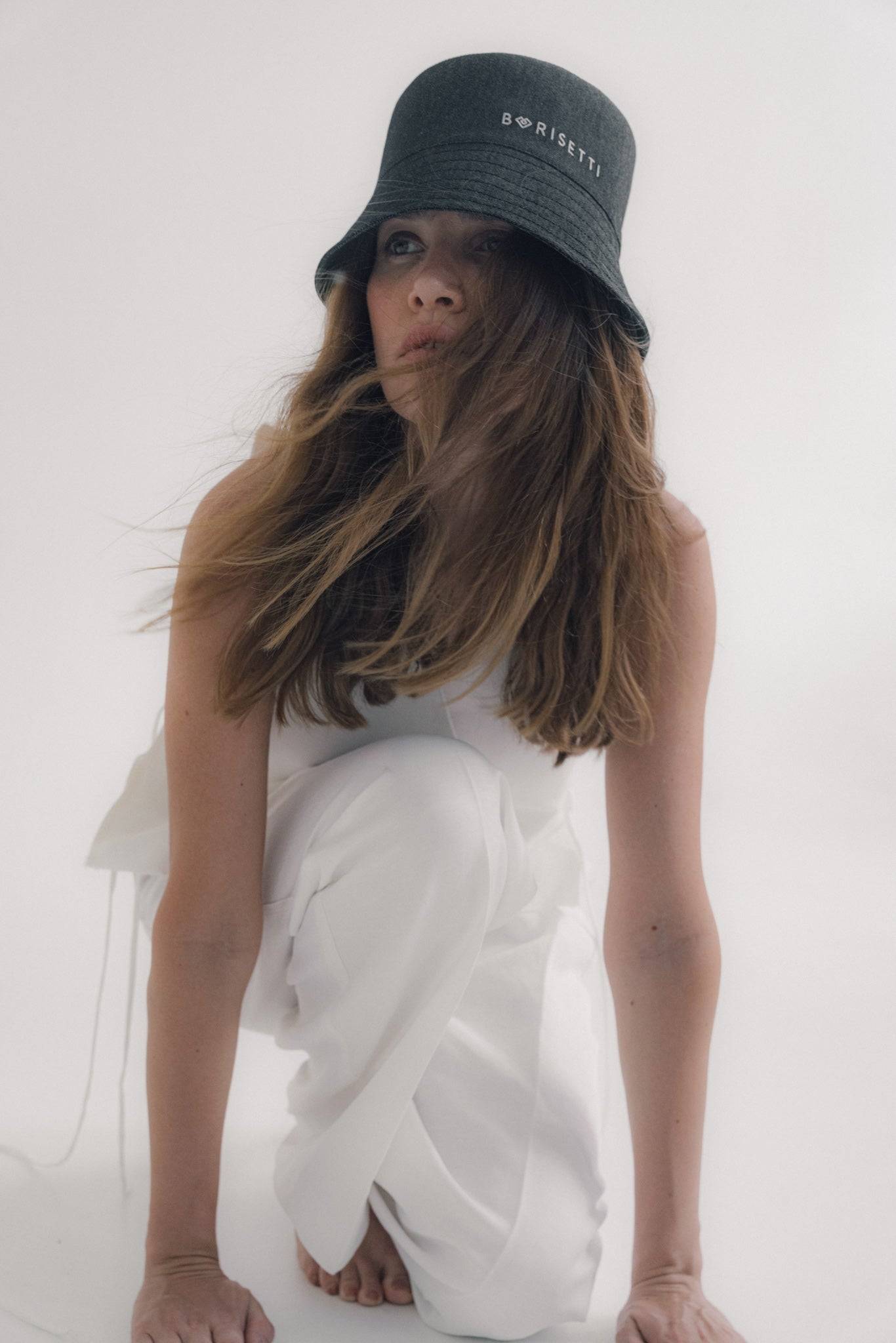 Black denim bucket hat with Borisetti embroidery, styled with a white sleeveless top. A modern and stylish accessory for any occasion.