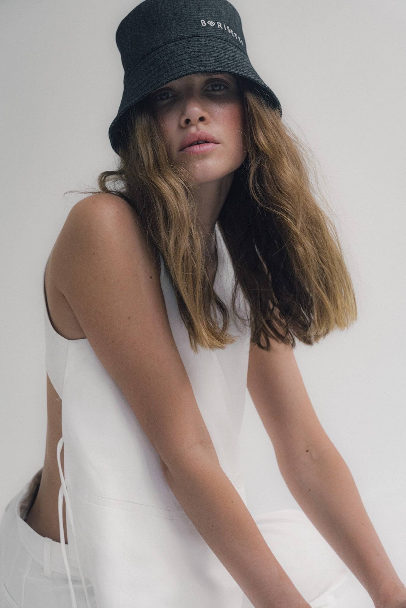 Minimalist black denim bucket hat with Borisetti branding, paired with a white outfit. A versatile and trendy fashion statement.