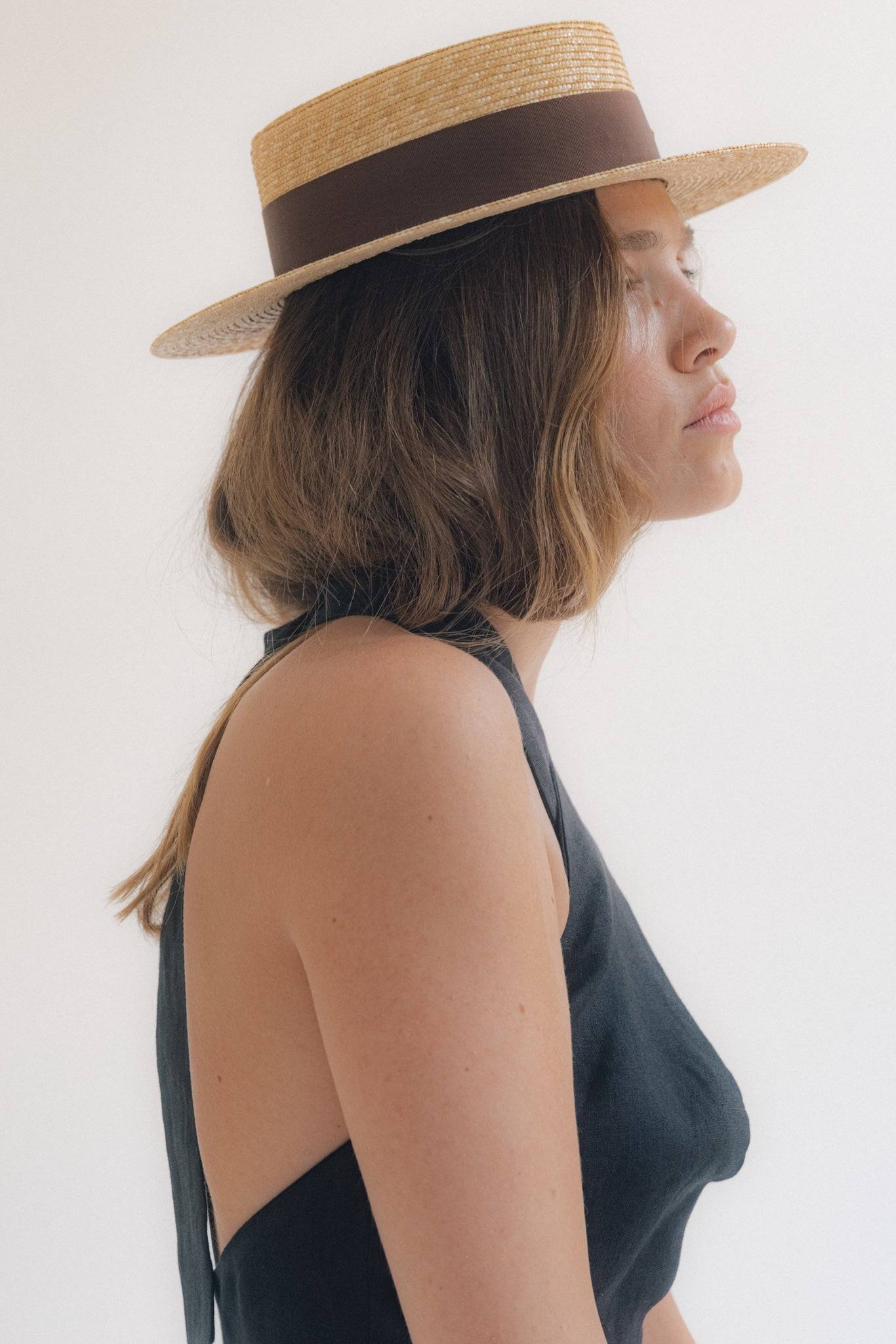 Side profile of a woman wearing a monogram-embellished straw boater hat with a brown ribbon, perfect for an elegant summer outfit.