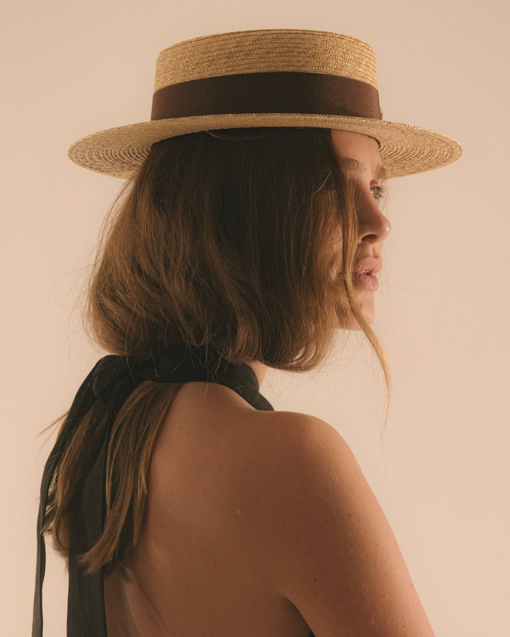 Back view of a monogram-embellished straw boater hat with a brown ribbon, highlighting its classic design for summer styling.