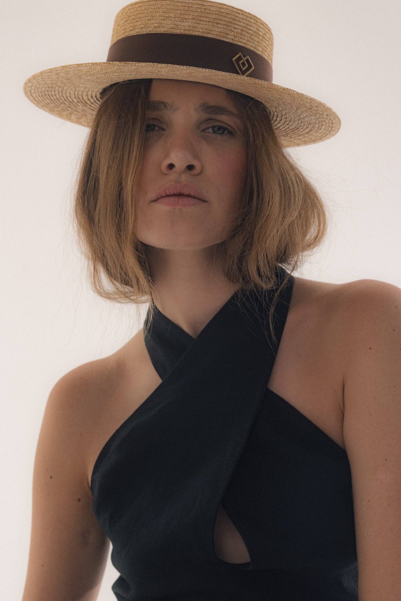 Close-up of a woman wearing a monogram-embellished straw boater hat, showcasing its elegant craftsmanship and summer-ready appeal.