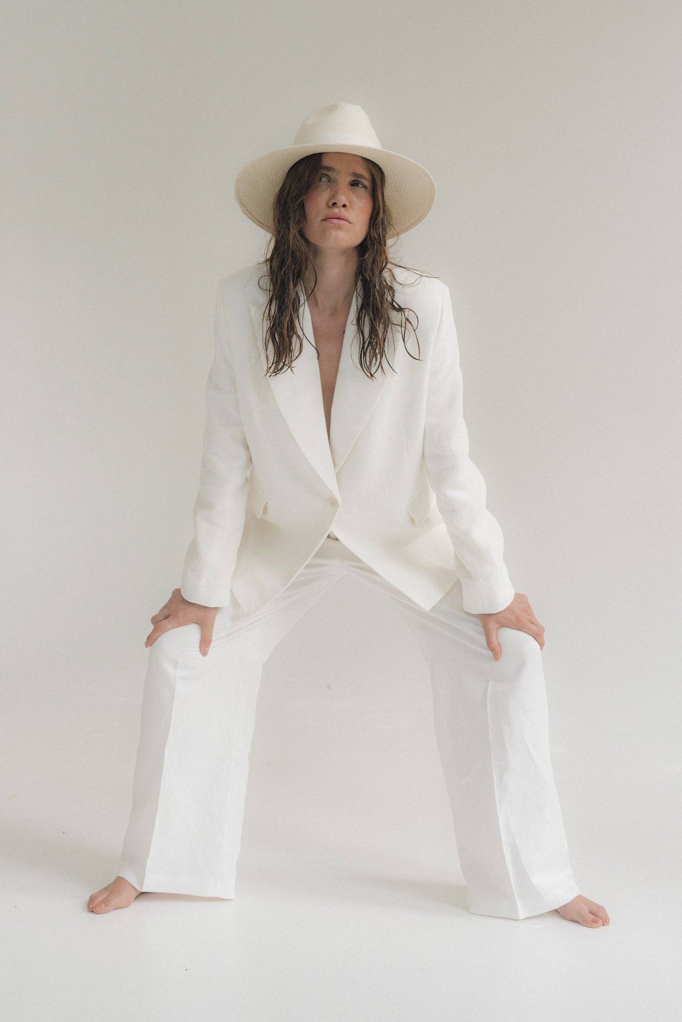 Minimalist fashion featuring a white wide-brimmed fedora hat and a tailored white suit. A handcrafted summer hat for a polished and stylish outfit.