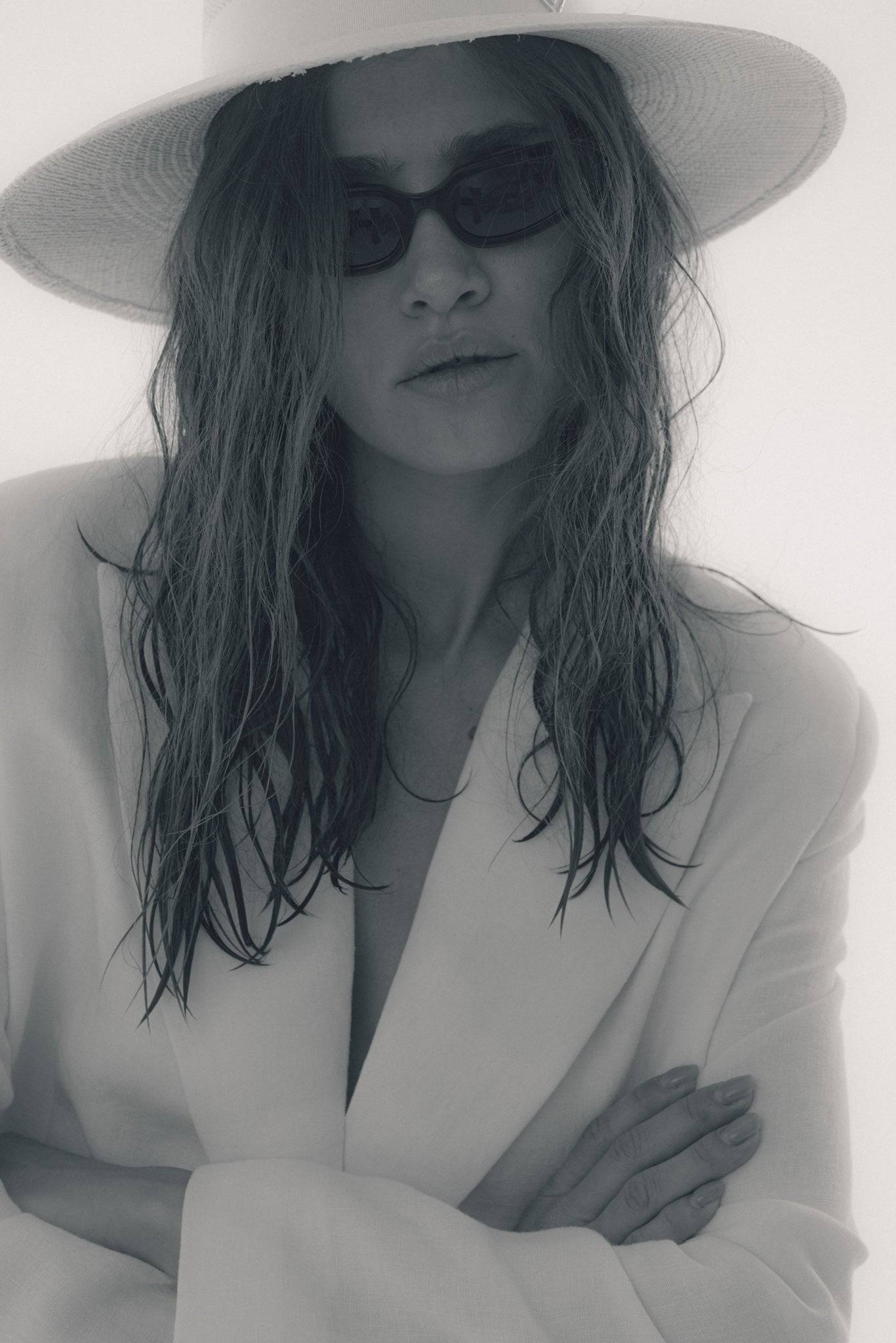 Monochrome close-up of a model in a white wide-brimmed fedora hat and sunglasses. A timeless and elegant handcrafted summer hat for any occasion.