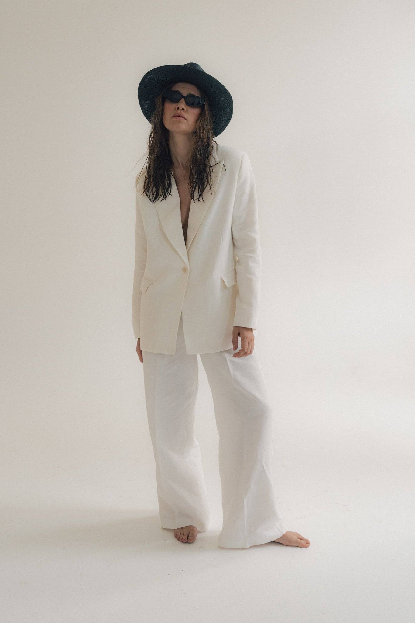 Model wearing a black fedora straw hat with a white linen suit, embodying effortless summer elegance and timeless fashion.