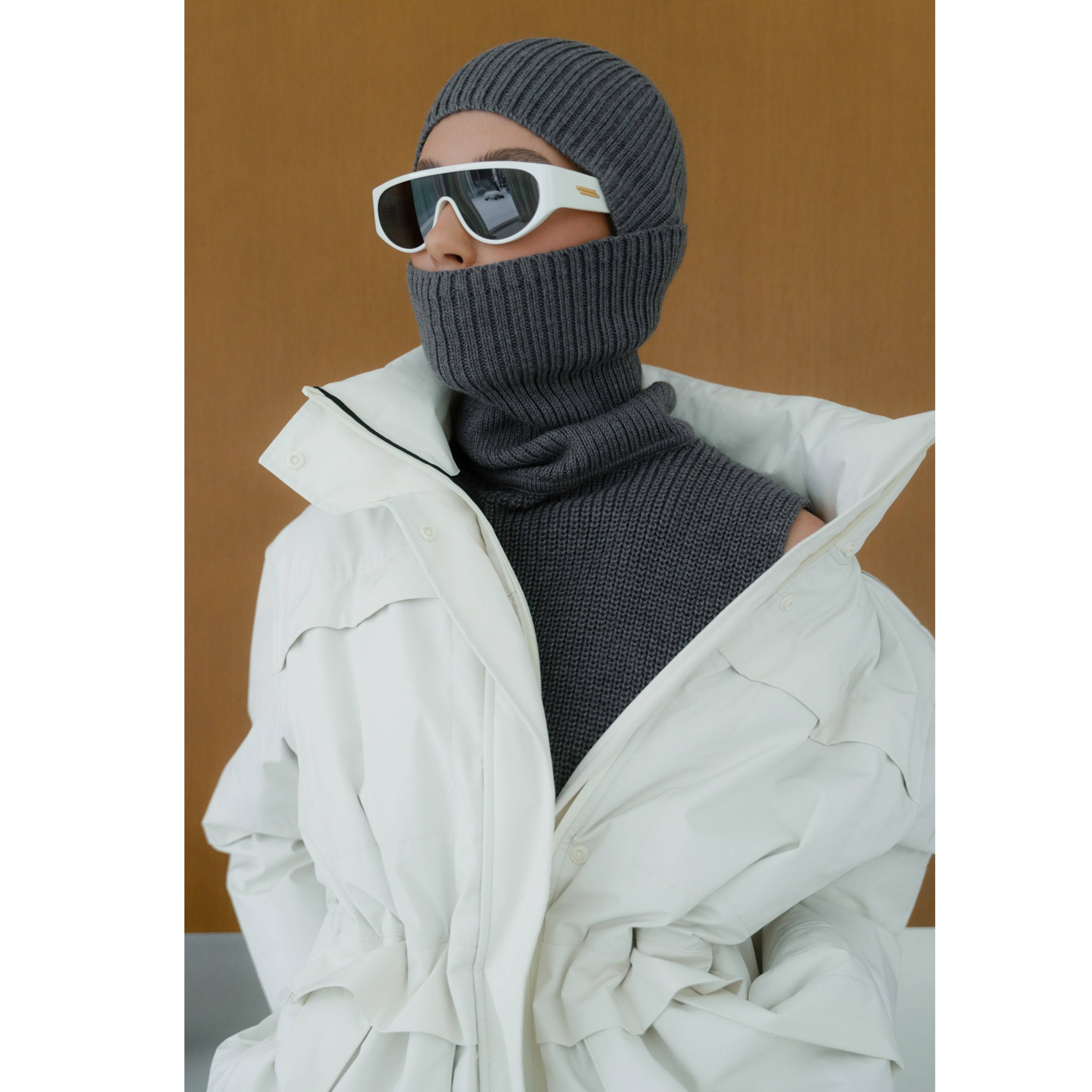 Merino wool dark grey balaclava styled with a white coat and sunglasses. A versatile two-piece knit accessory for winter fashion.