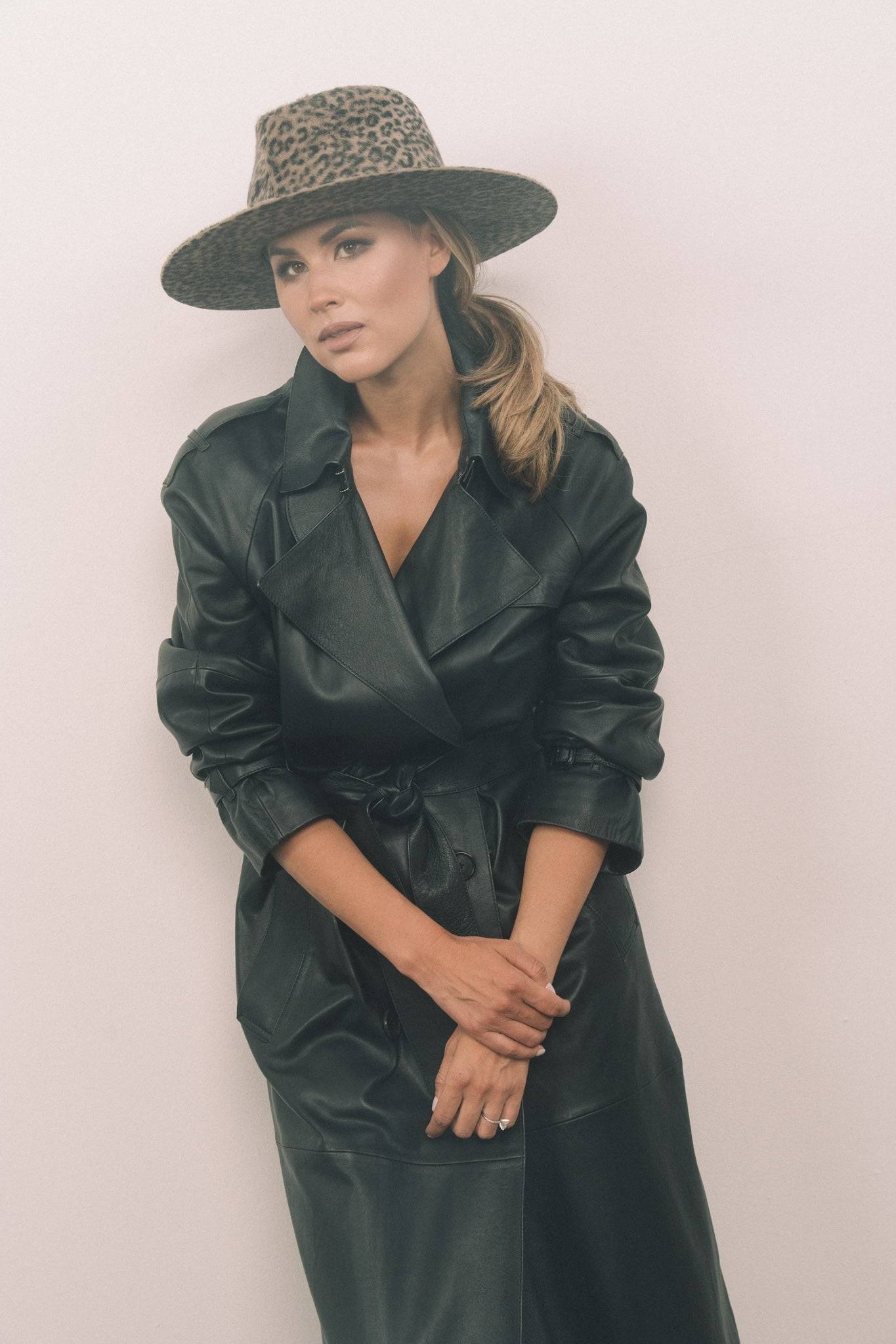 Woman wearing a brown leopard print fedora hat with a black leather trench coat. A high-fashion accessory for casual to formal wear.
