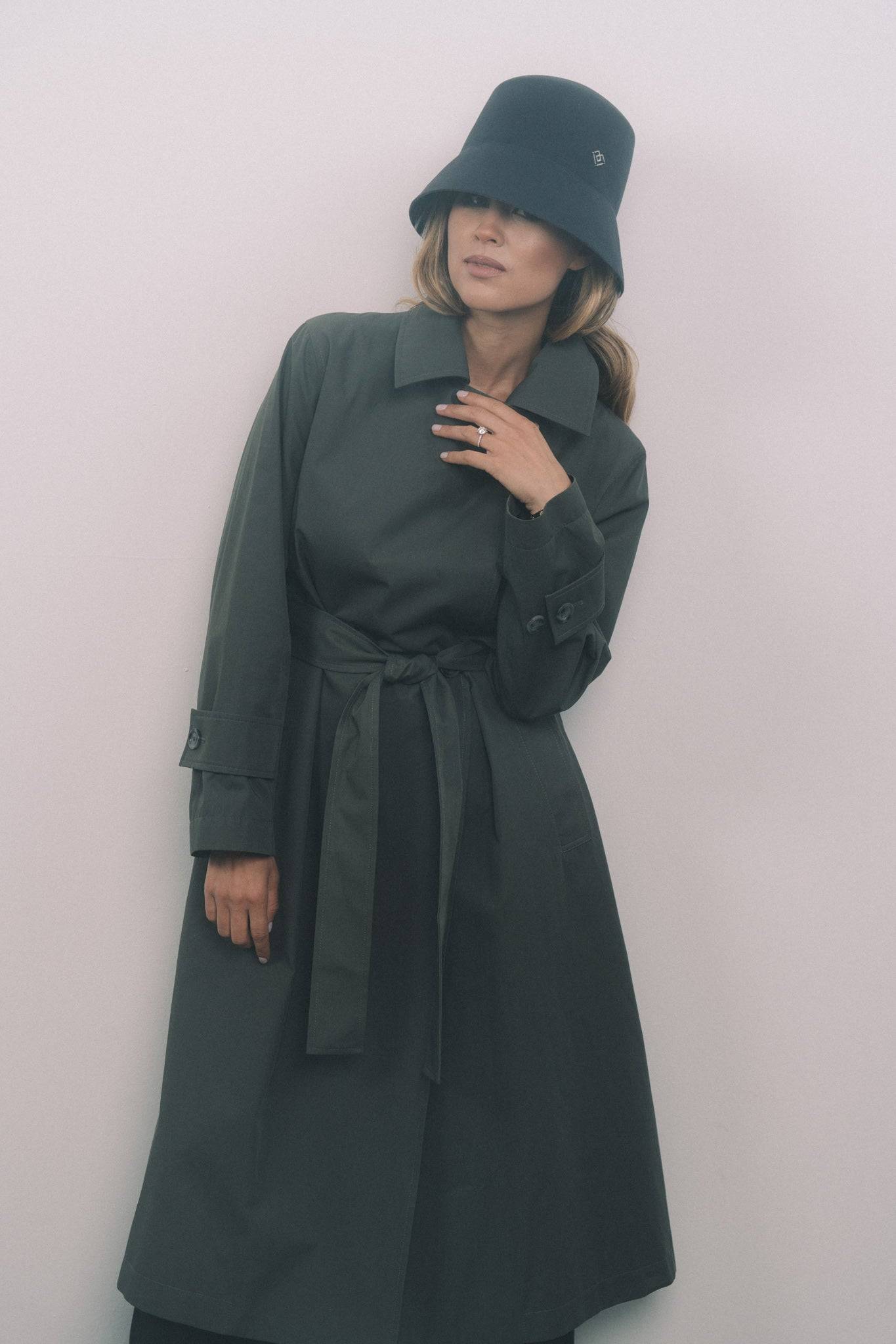 Dark grey bucket hat handcrafted from 100% fur felt, featuring a heart monogram. Styled with a belted trench coat for a chic, modern look.