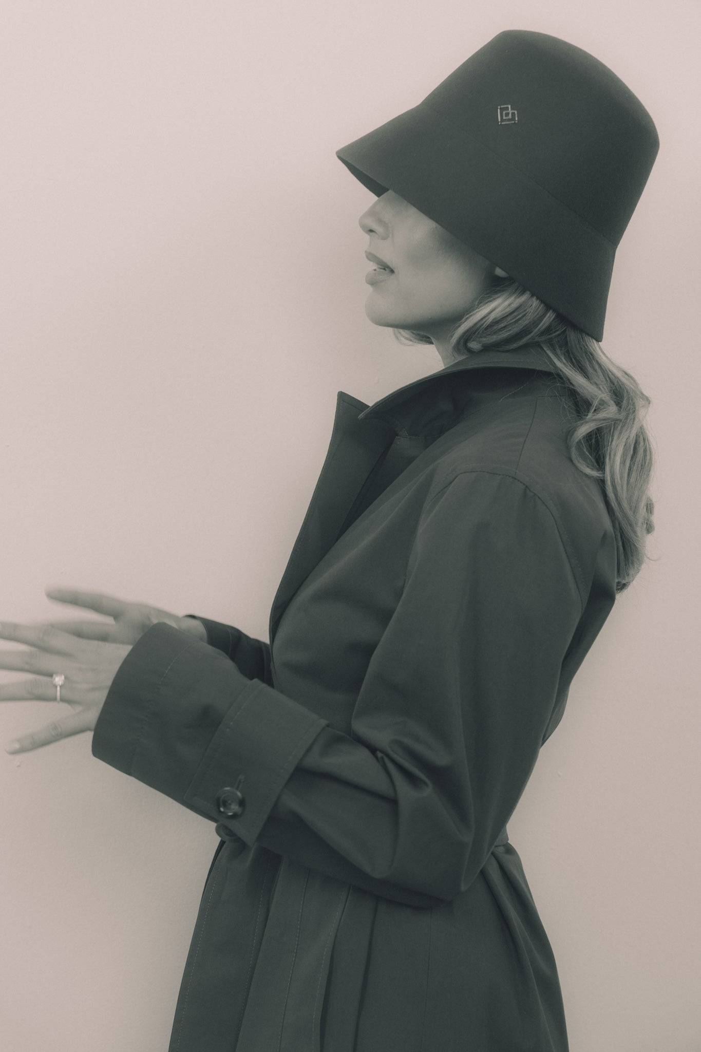 Monochrome side profile of a woman wearing a dark grey fur felt bucket hat with a heart monogram. A timeless and sophisticated fashion statement.