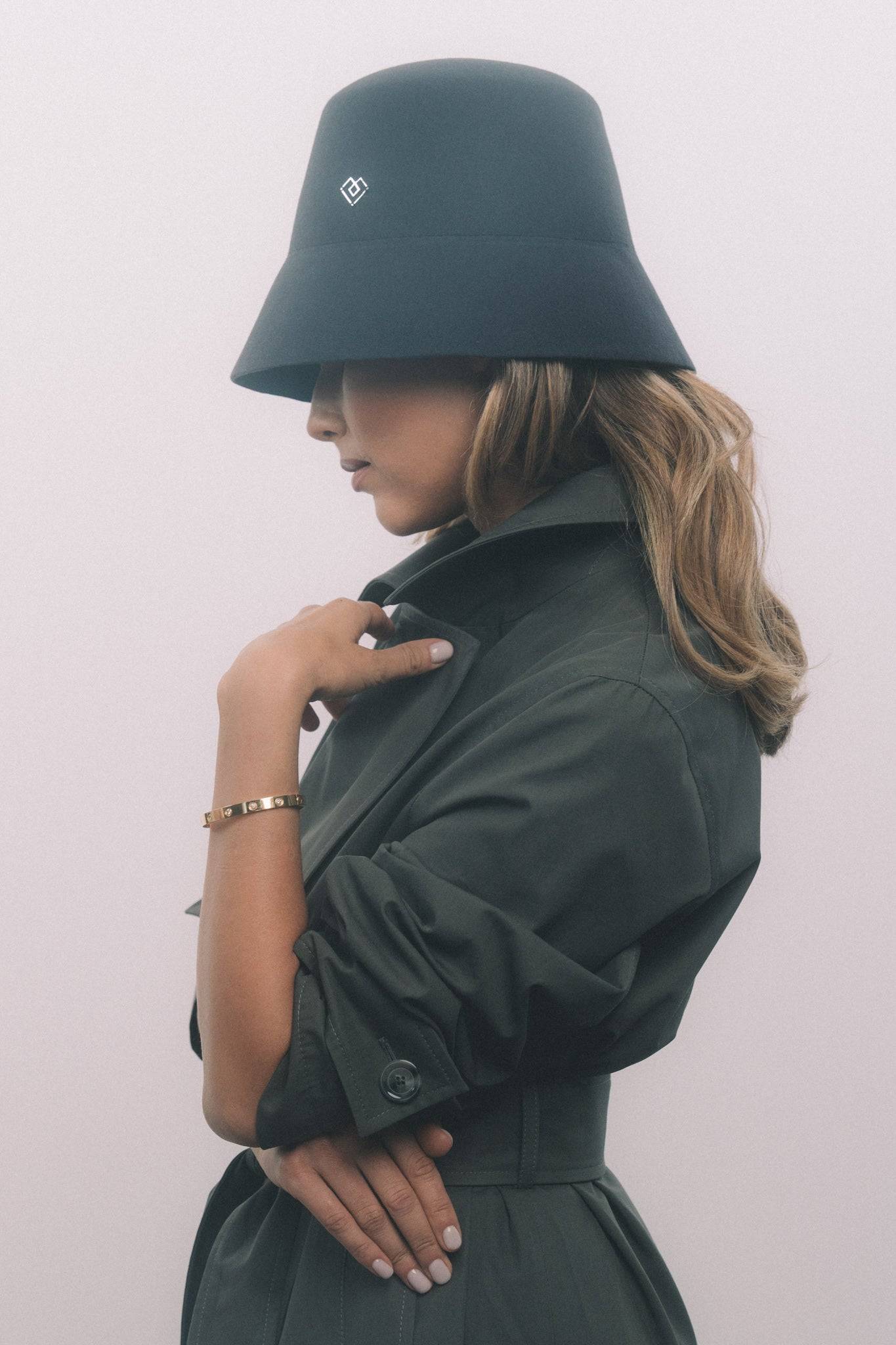 Stylish dark grey bucket hat with a structured silhouette and heart monogram, paired with a classic trench coat. A perfect blend of elegance and modernity.