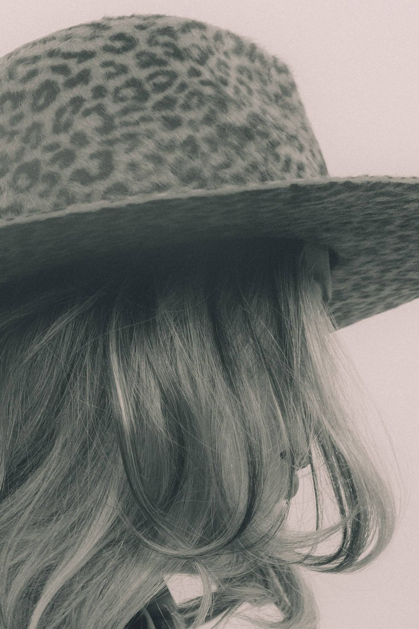 Close-up of a brown leopard print fedora hat with soft waves of blonde hair. A handcrafted luxury accessory for a statement look.