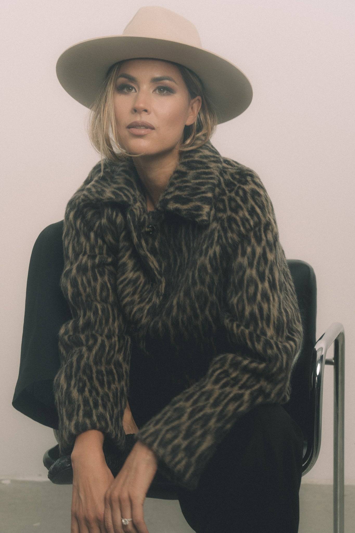 Elegant cream fedora hat with a wide brim, worn by a model in a leopard-print coat. Shop the Borisetti Heart Monogram Fedora for a timeless look.