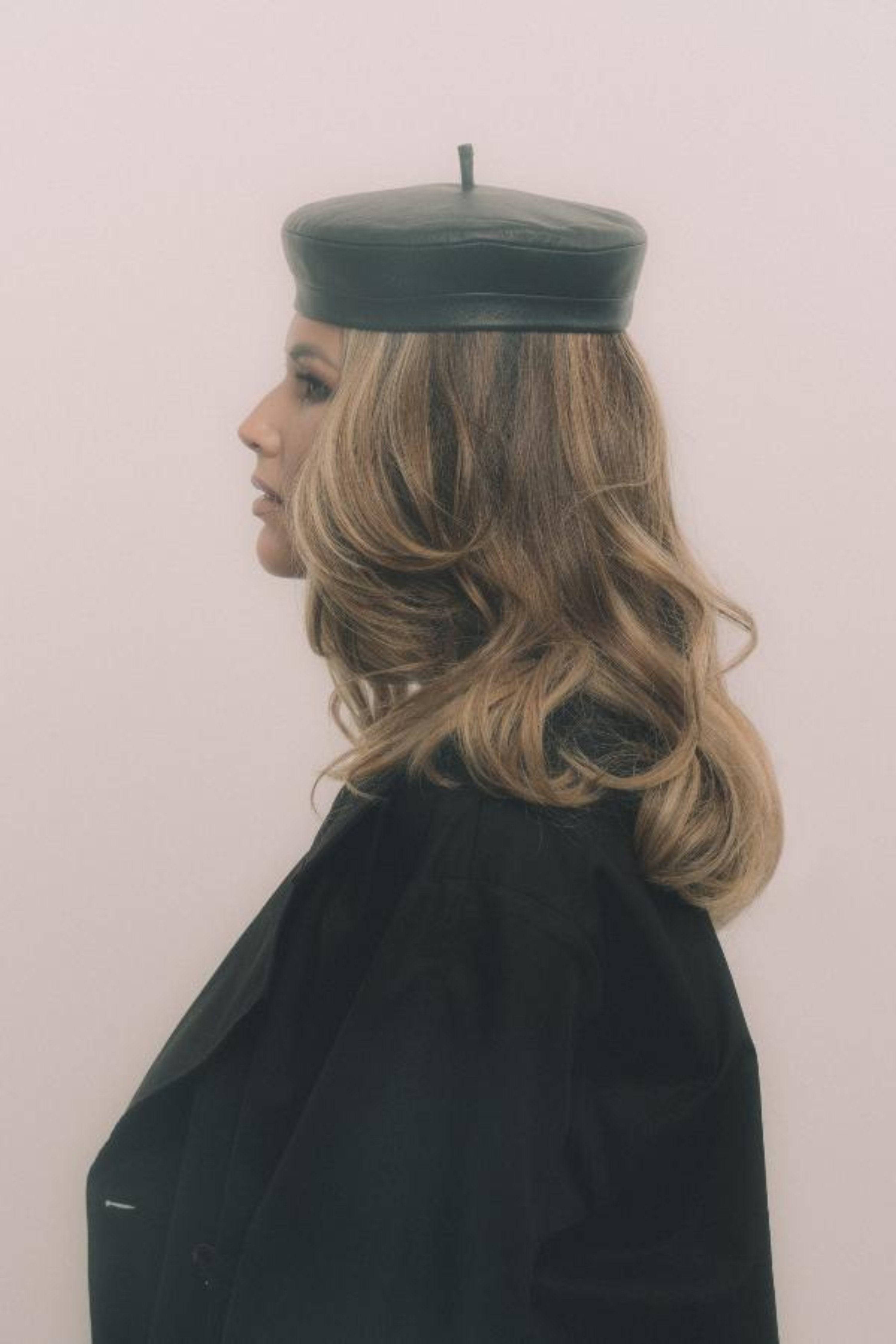 Black leather beret styled with a dark trench coat, showcasing a chic Parisian look. Handcrafted design with a heart monogram detail.