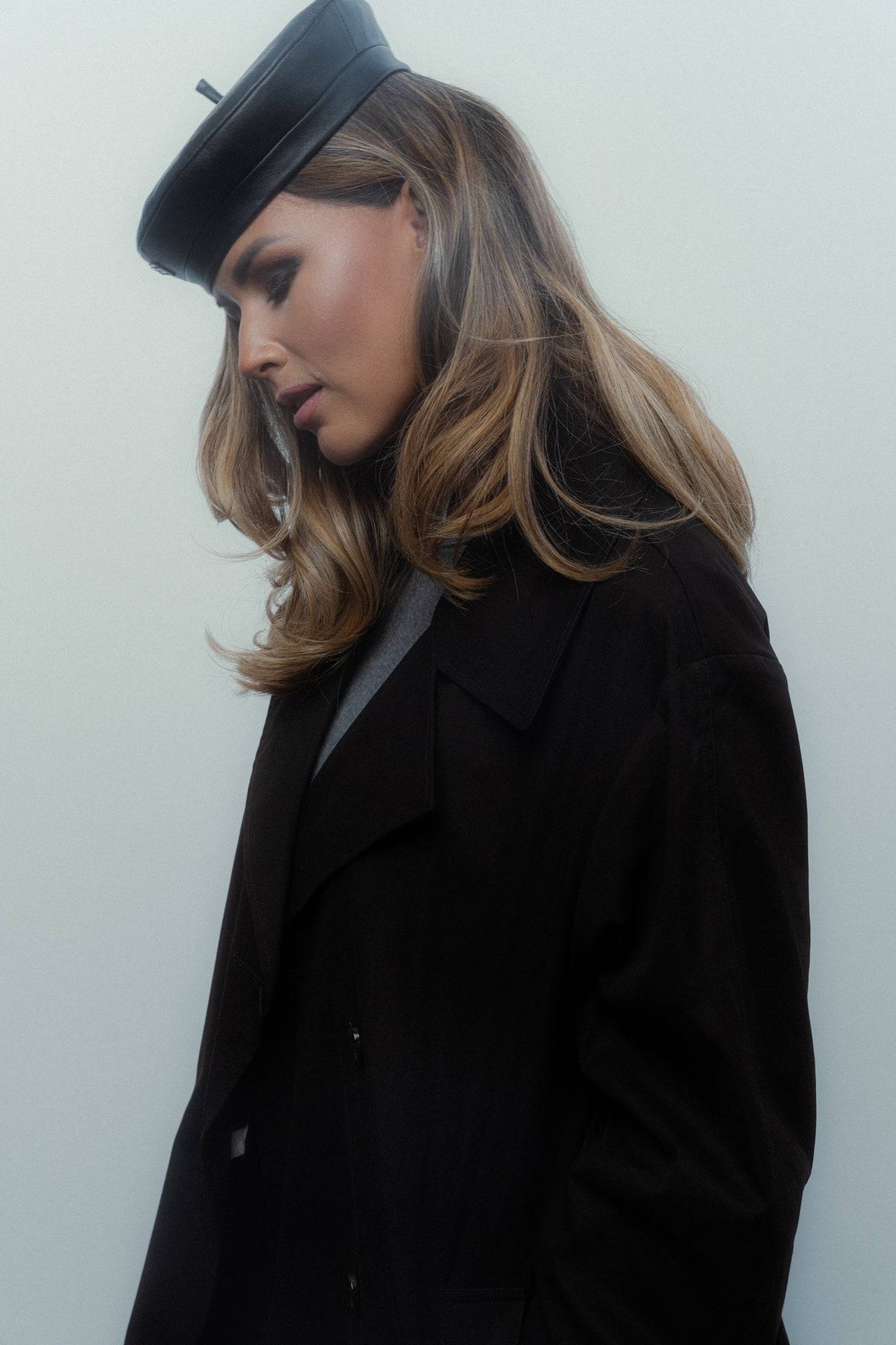 Side profile of a woman wearing a black leather beret, highlighting its structured design. A modern take on classic Parisian fashion.