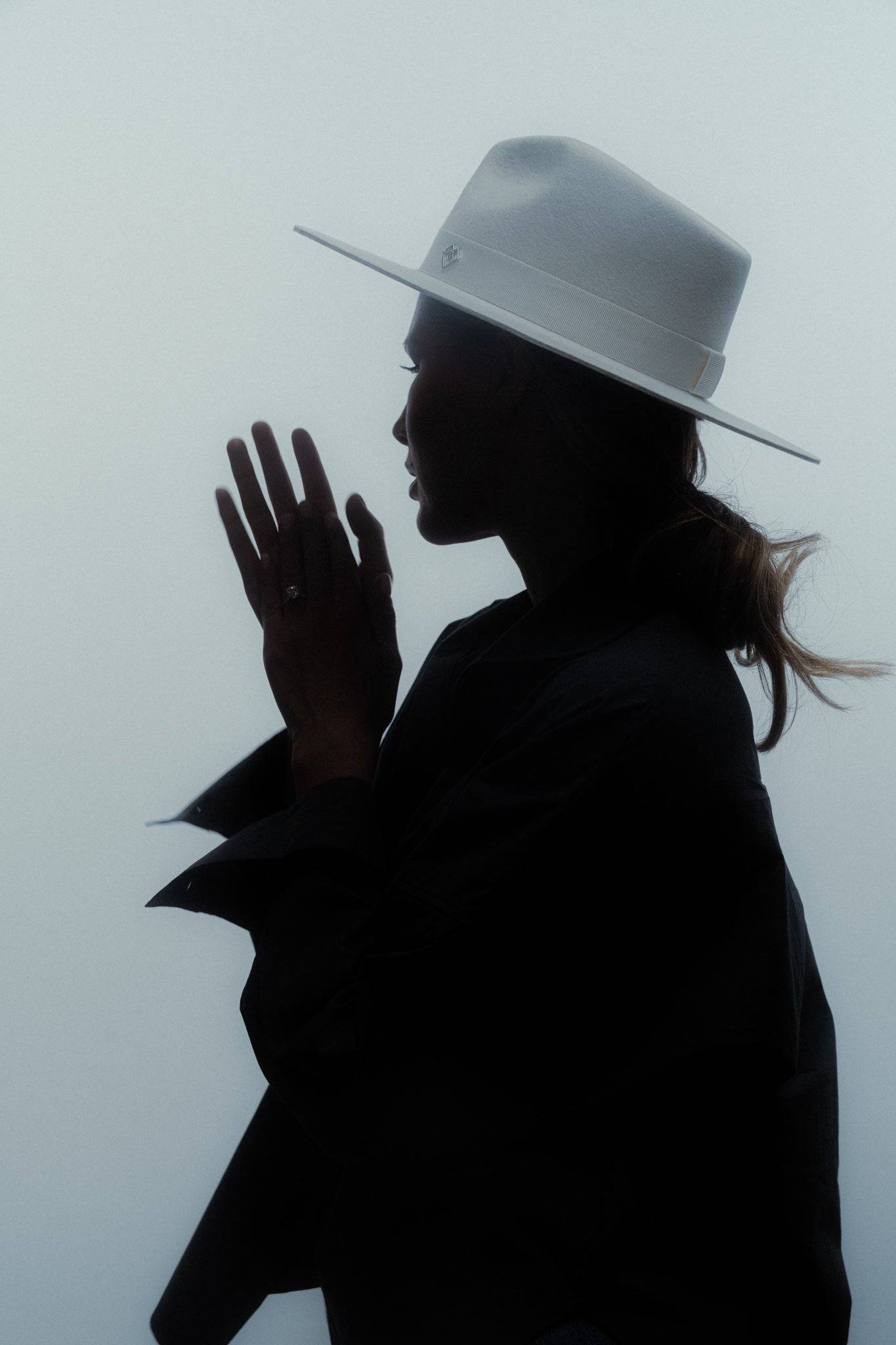 Silhouette of a woman wearing an ivory fedora hat, emphasizing its structured design and timeless elegance in a moody lighting setting.