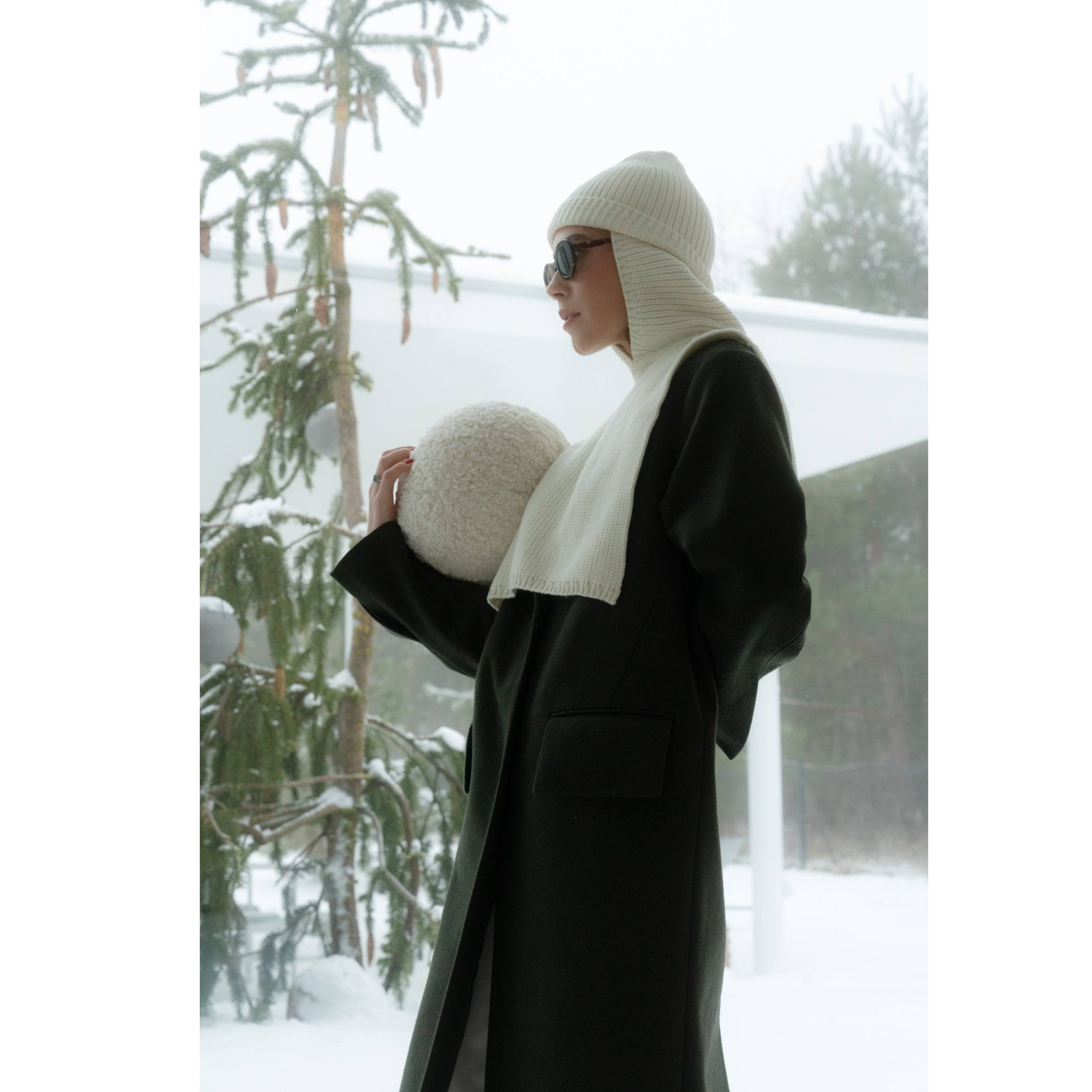 Model wearing a milky white two-piece Merino wool balaclava by Borisetti Atelier, paired with a dark coat in a snowy outdoor setting.