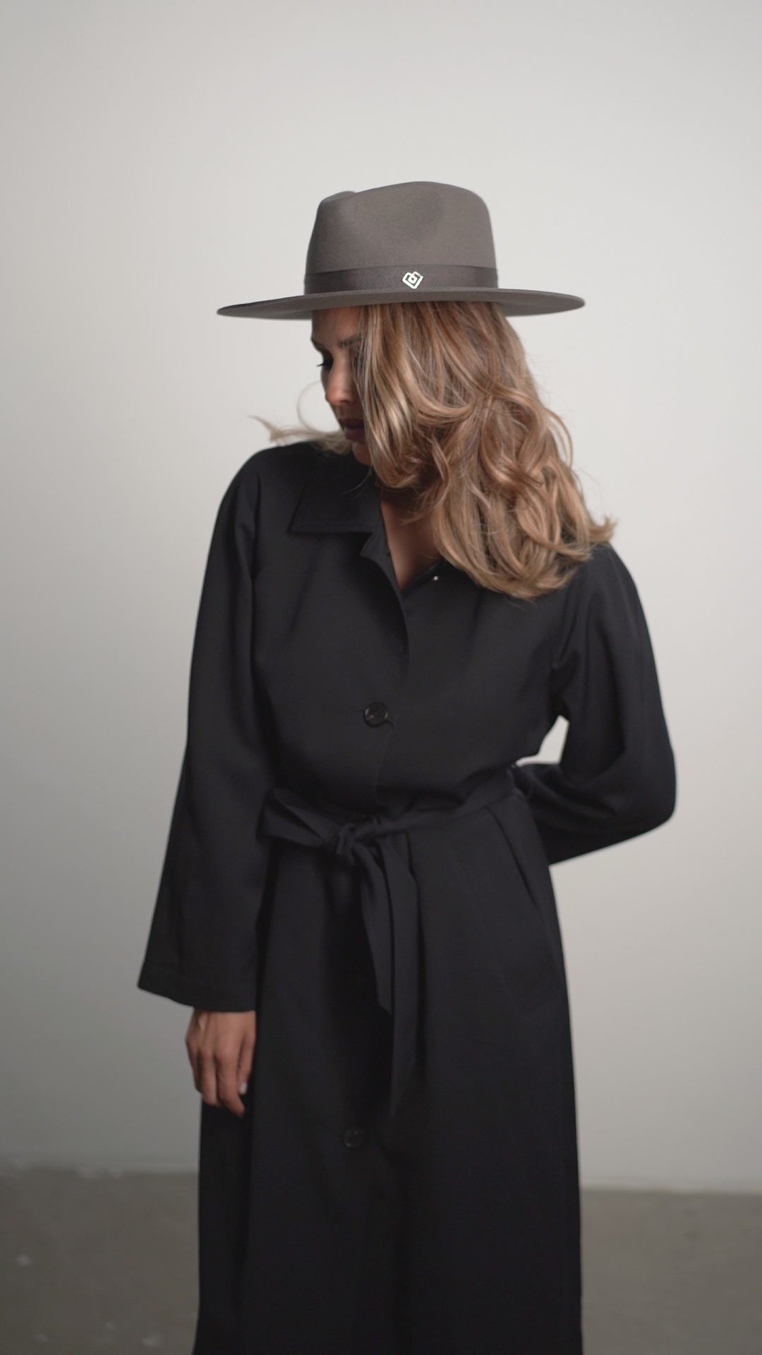 Designer grey fedora hat with monogram detail, paired with a black coat. A luxury handcrafted accessory for a high-fashion statement. Order today.
